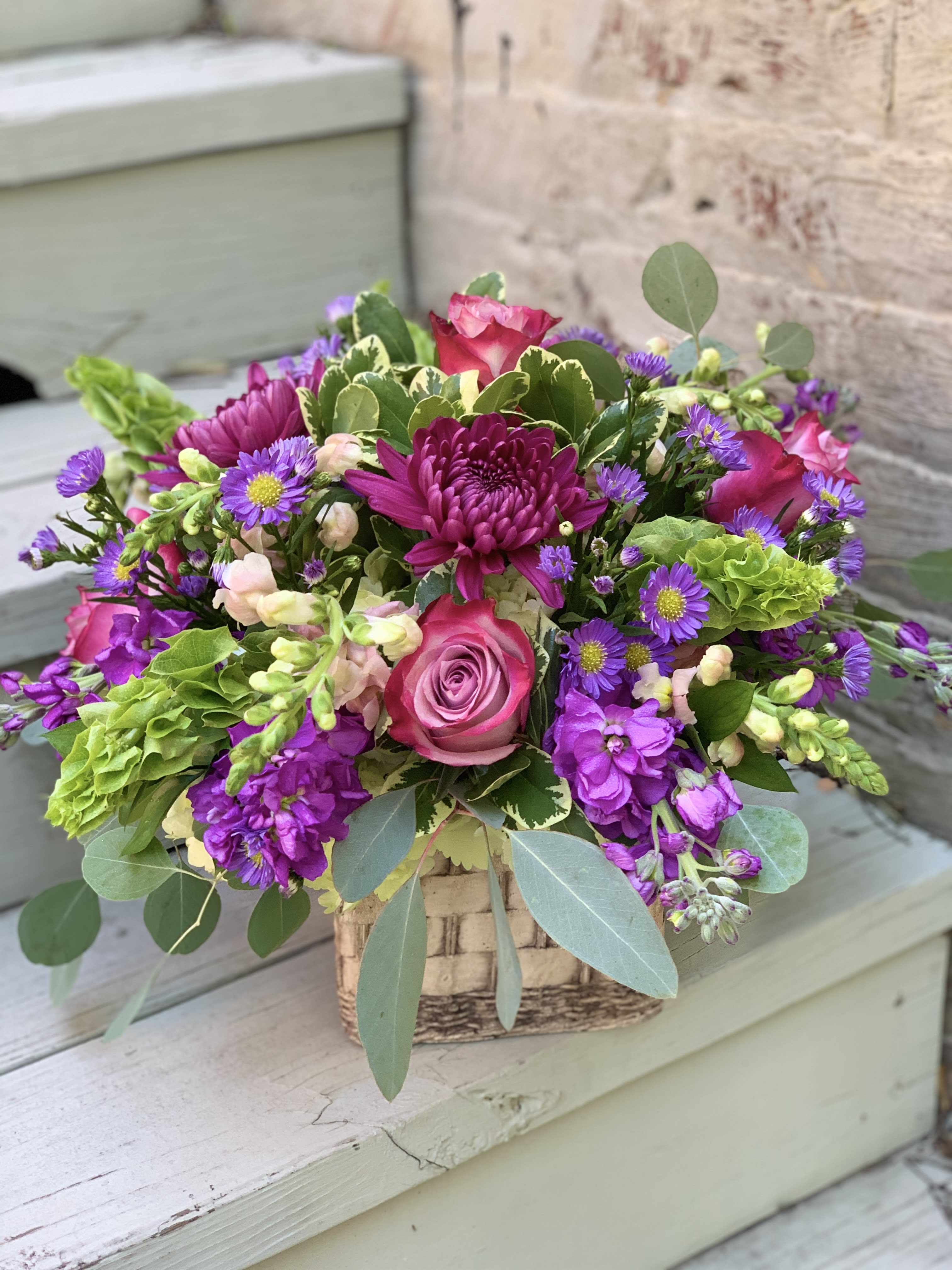 Mixed pink and purple flower arrangement in a woven basket
