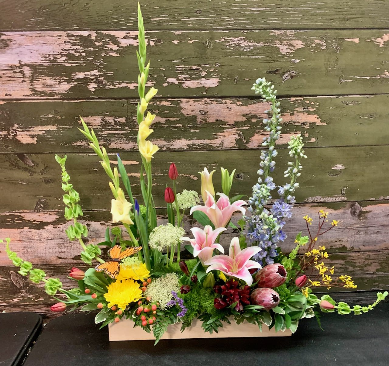 Mixed floral arrangement in a rectangular wooden box with lilies and tall spikes