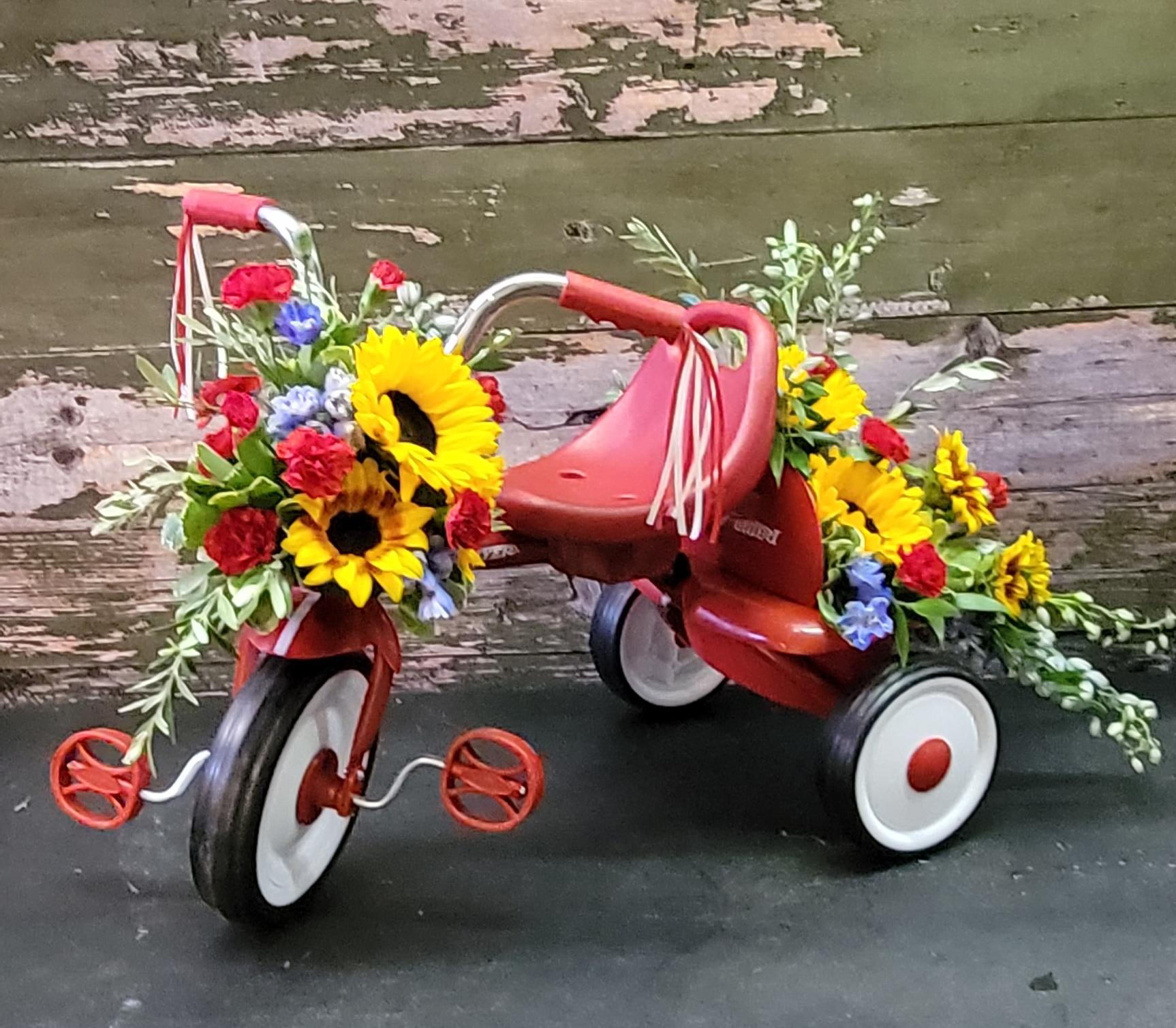 Flower-covered red tricycle with sunflowers and mixed blooms