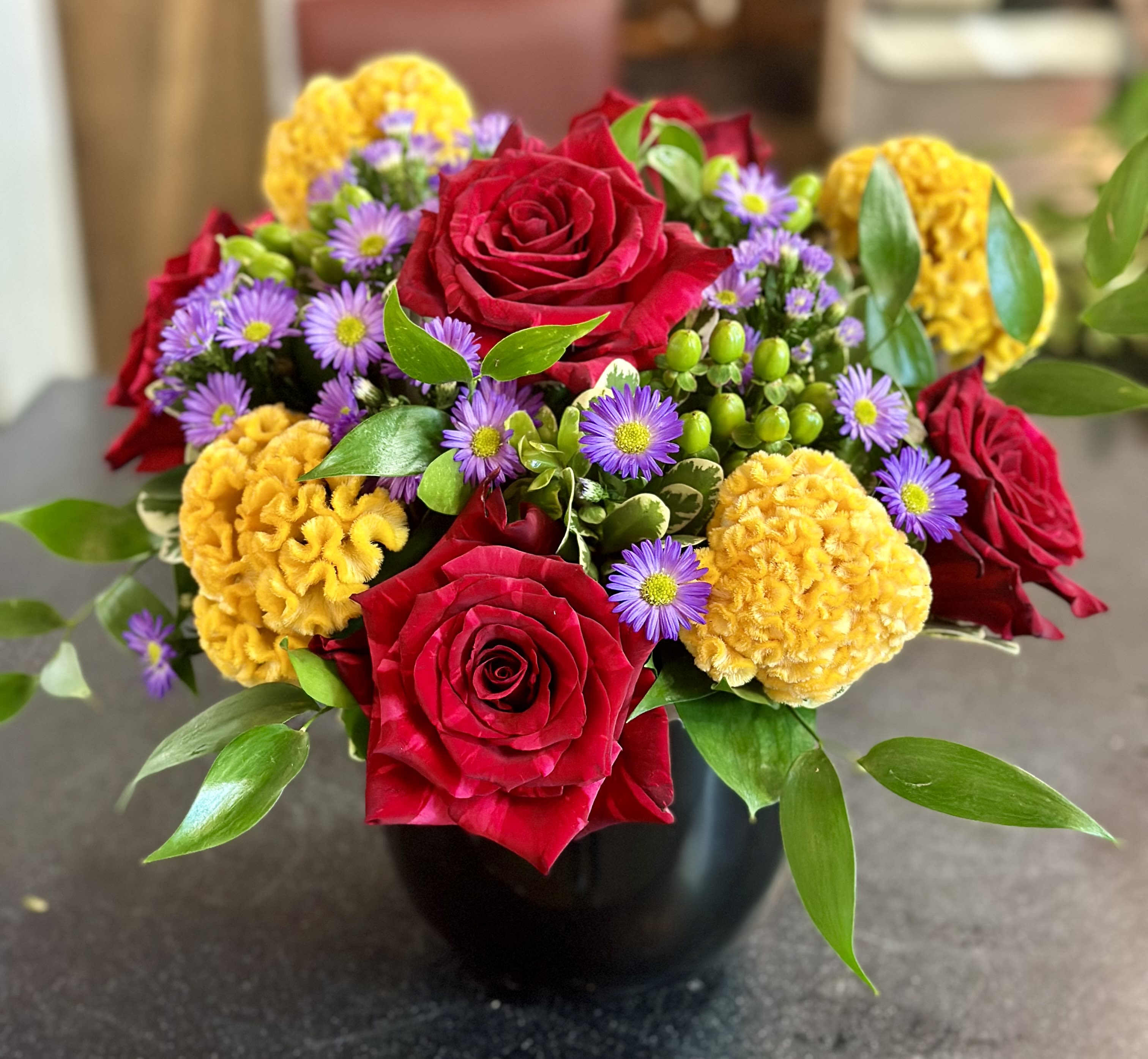 Bouquet of red roses, purple daisies, and yellow blooms in a black vase