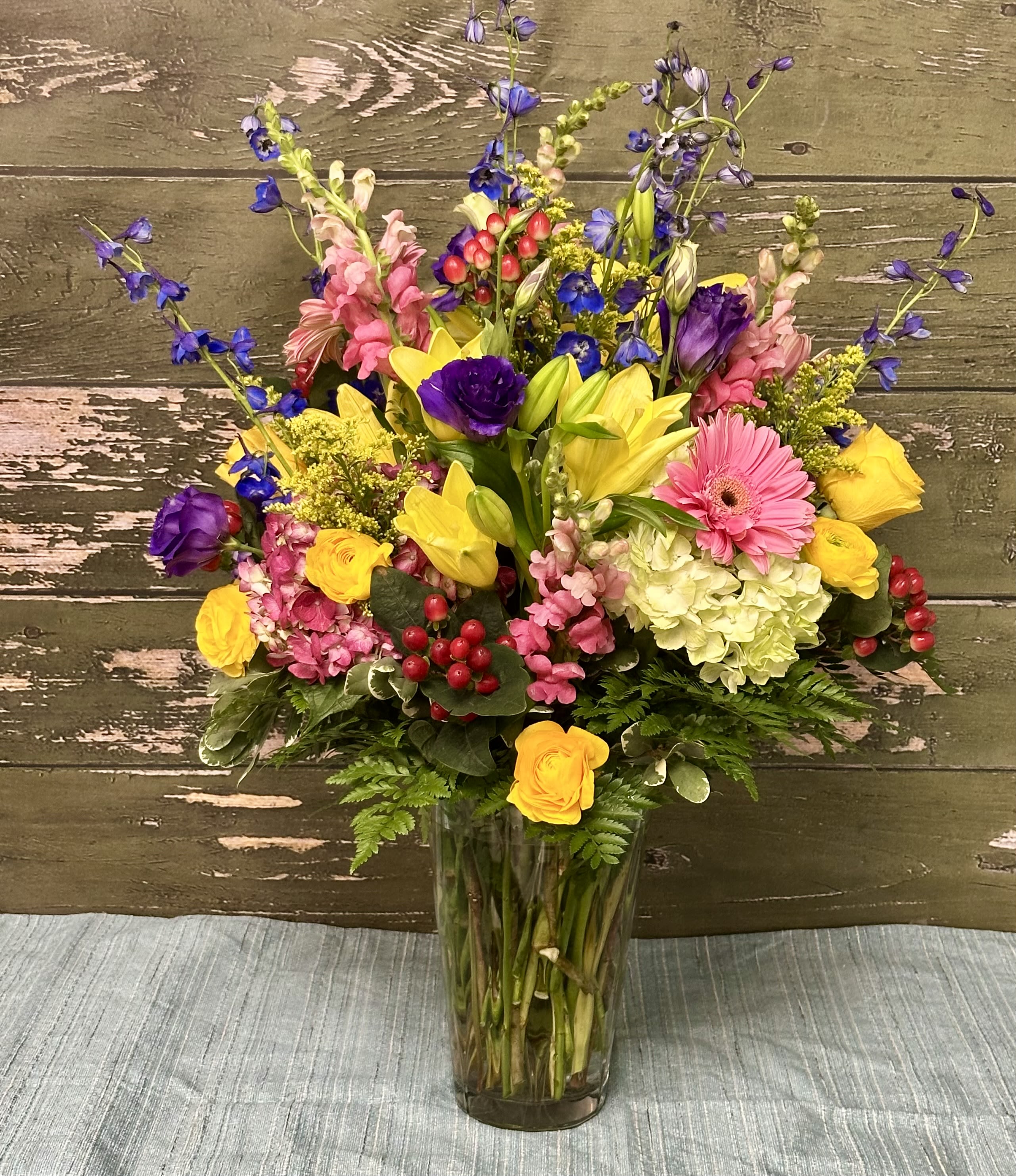 Mixed bouquet in a clear glass vase with yellow, pink, purple, and blue flowers