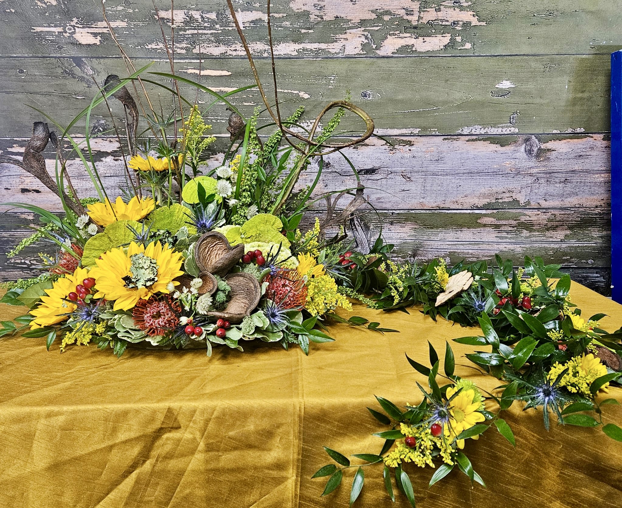 Yellow floral arrangement with greenery and decorative pods on a table