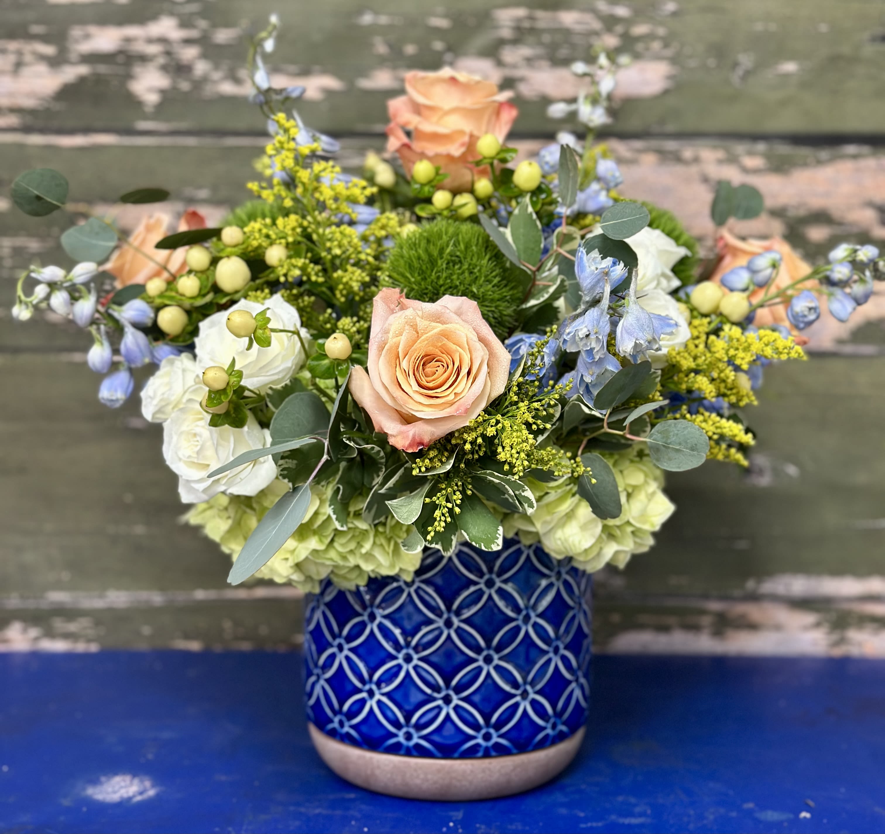 Mixed bouquet of peach roses, white blooms, and blue flowers in a patterned blue vase