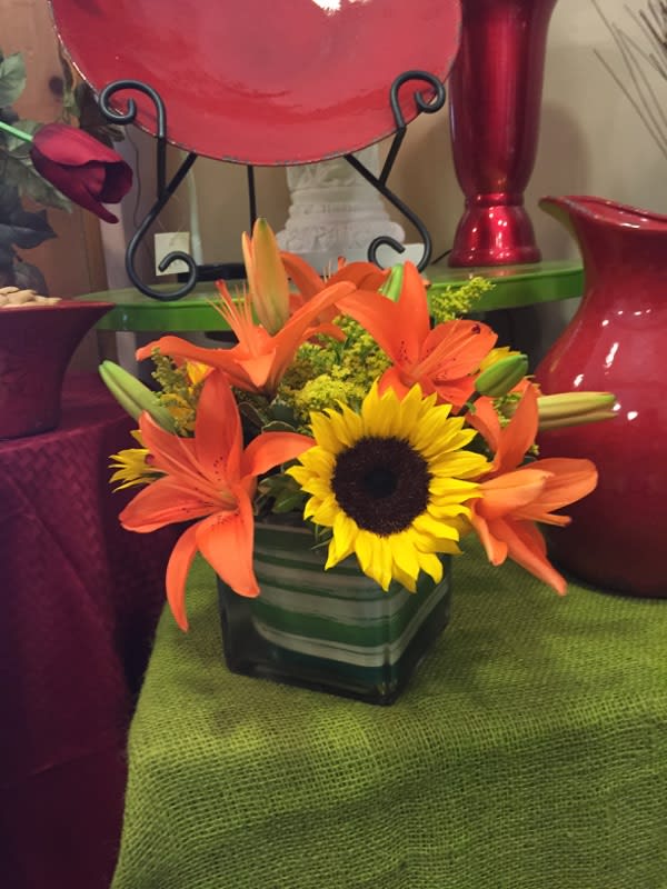 Orange lilies and a sunflower in a square glass vase