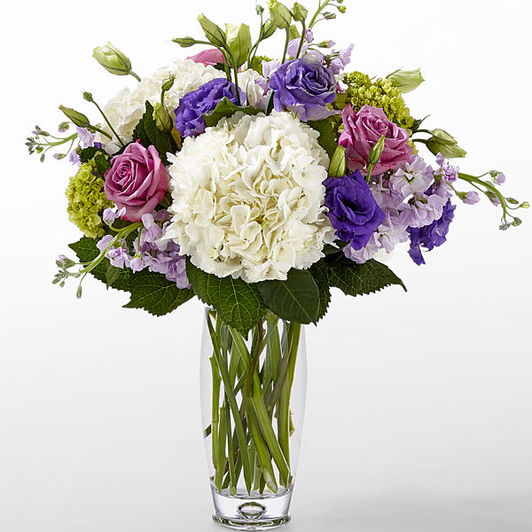 Bouquet of white hydrangea, purple and pink roses in a clear glass vase