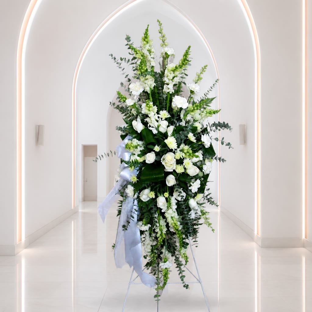 Tall white floral standing spray with ribbon in a bright hallway