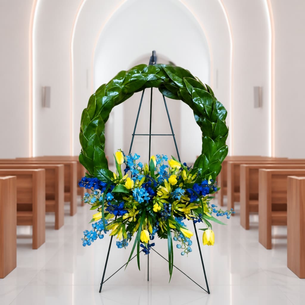 Large floral wreath on a stand with blue and yellow flowers in a church aisle