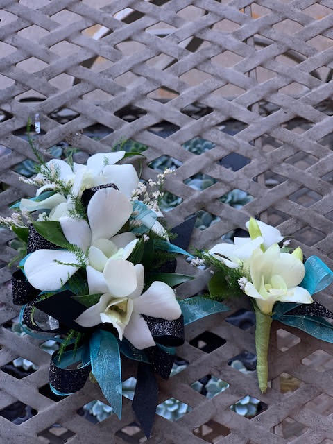 Two white floral corsages with teal ribbon accents on a lattice table