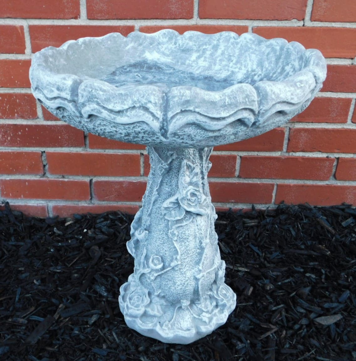 Stone birdbath with rose relief against a brick wall