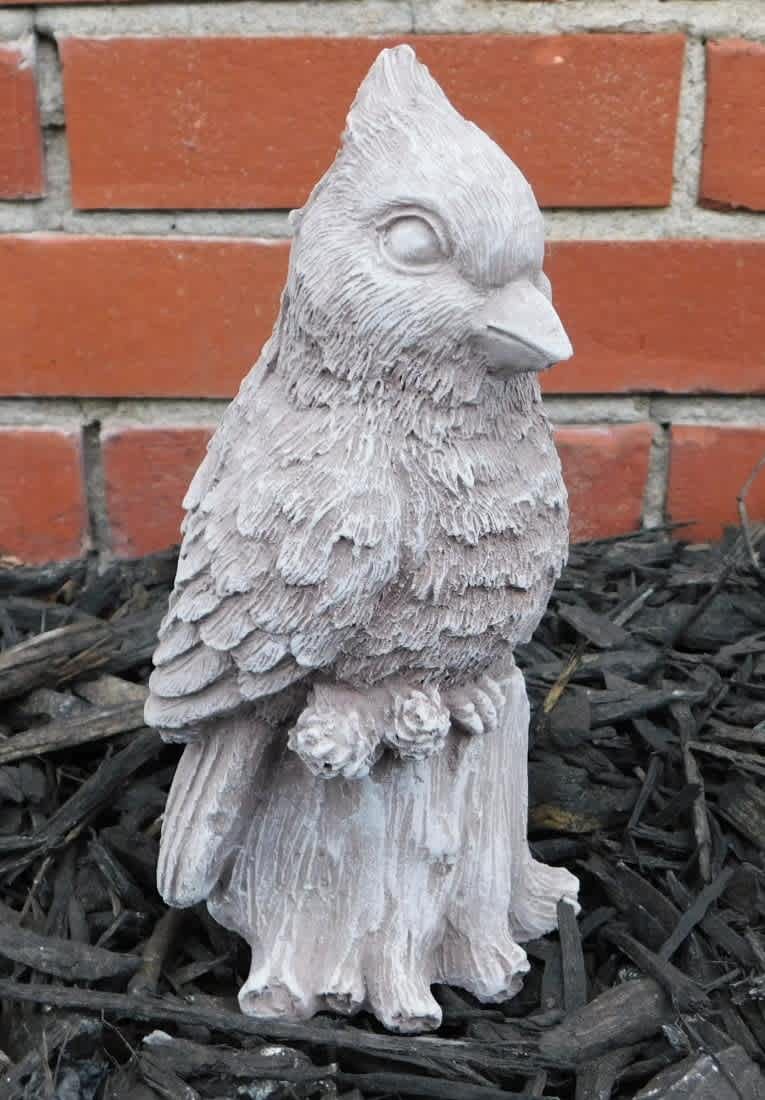 Small bird-shaped garden statue in front of a brick wall