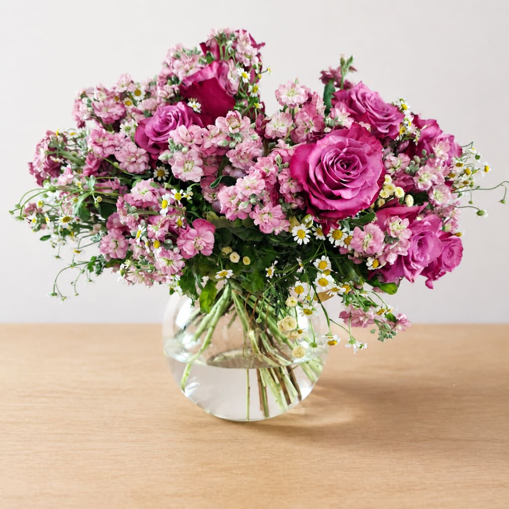 Pink roses and small pink flowers arranged in a clear glass vase