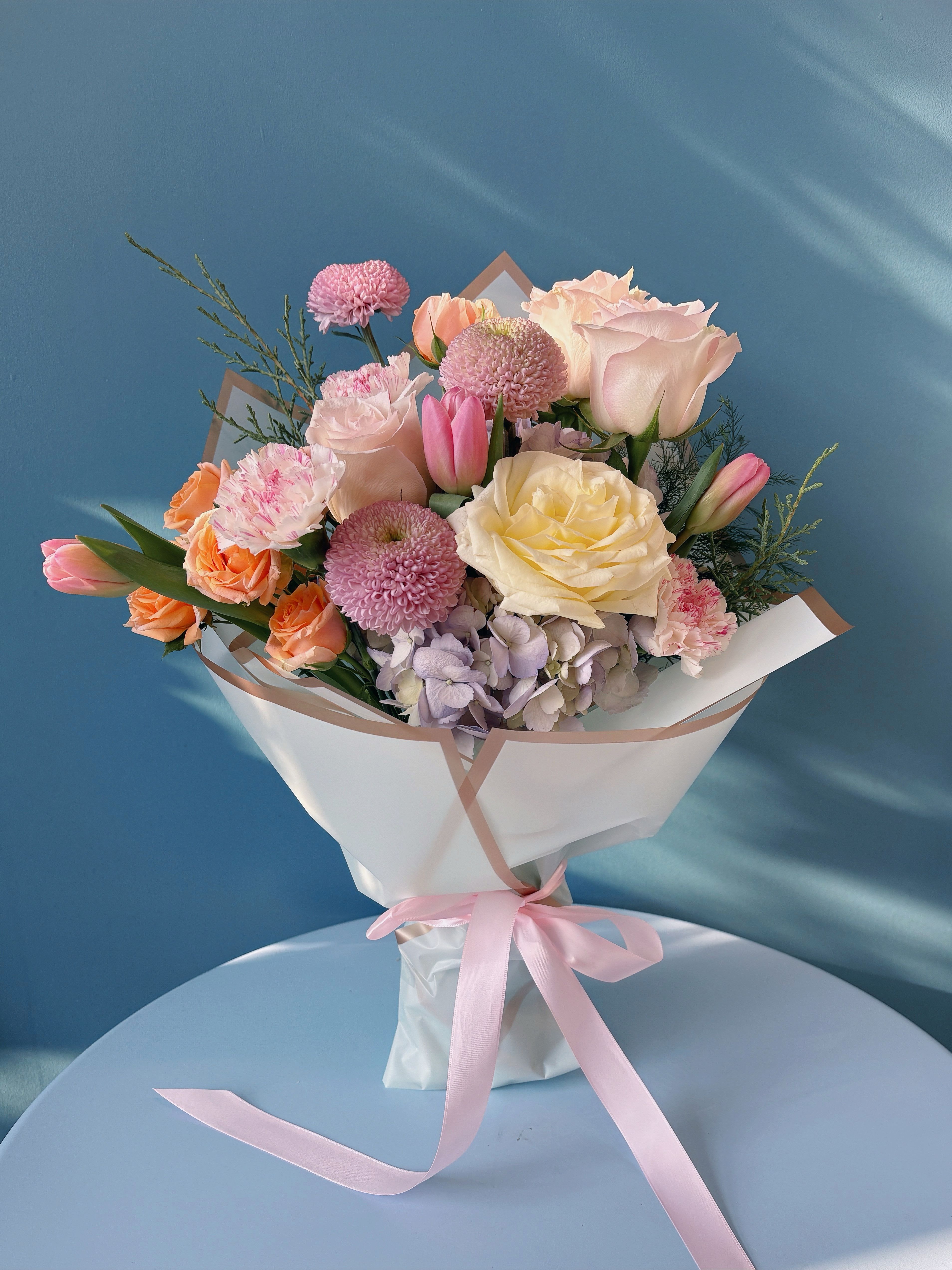 Pastel bouquet of roses, tulips, and chrysanthemums wrapped in white paper