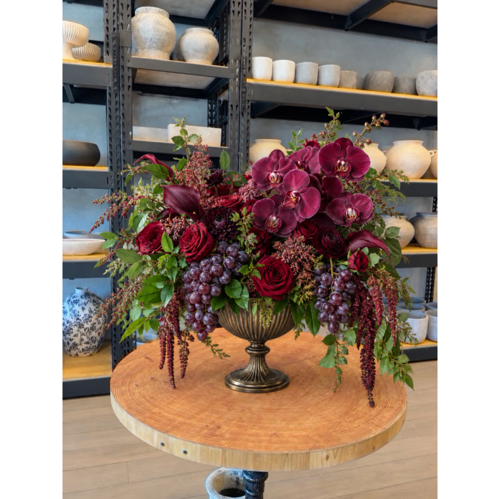 Deep red floral arrangement in a pedestal vase with hanging grape clusters