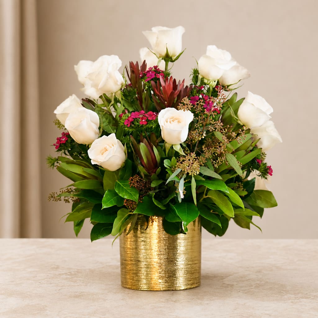 White roses arranged in a gold vase with pink accents