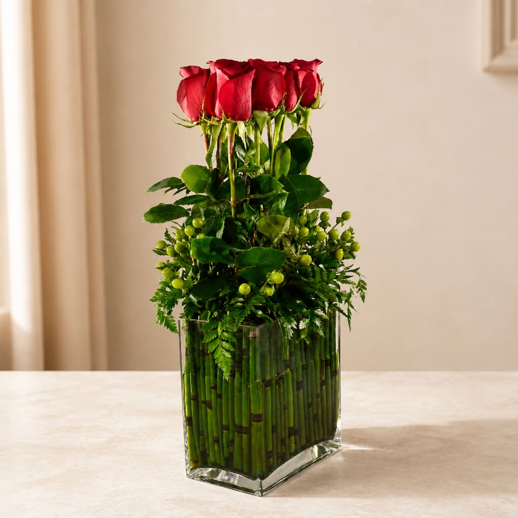 Red roses arranged in a tall glass vase with green accents