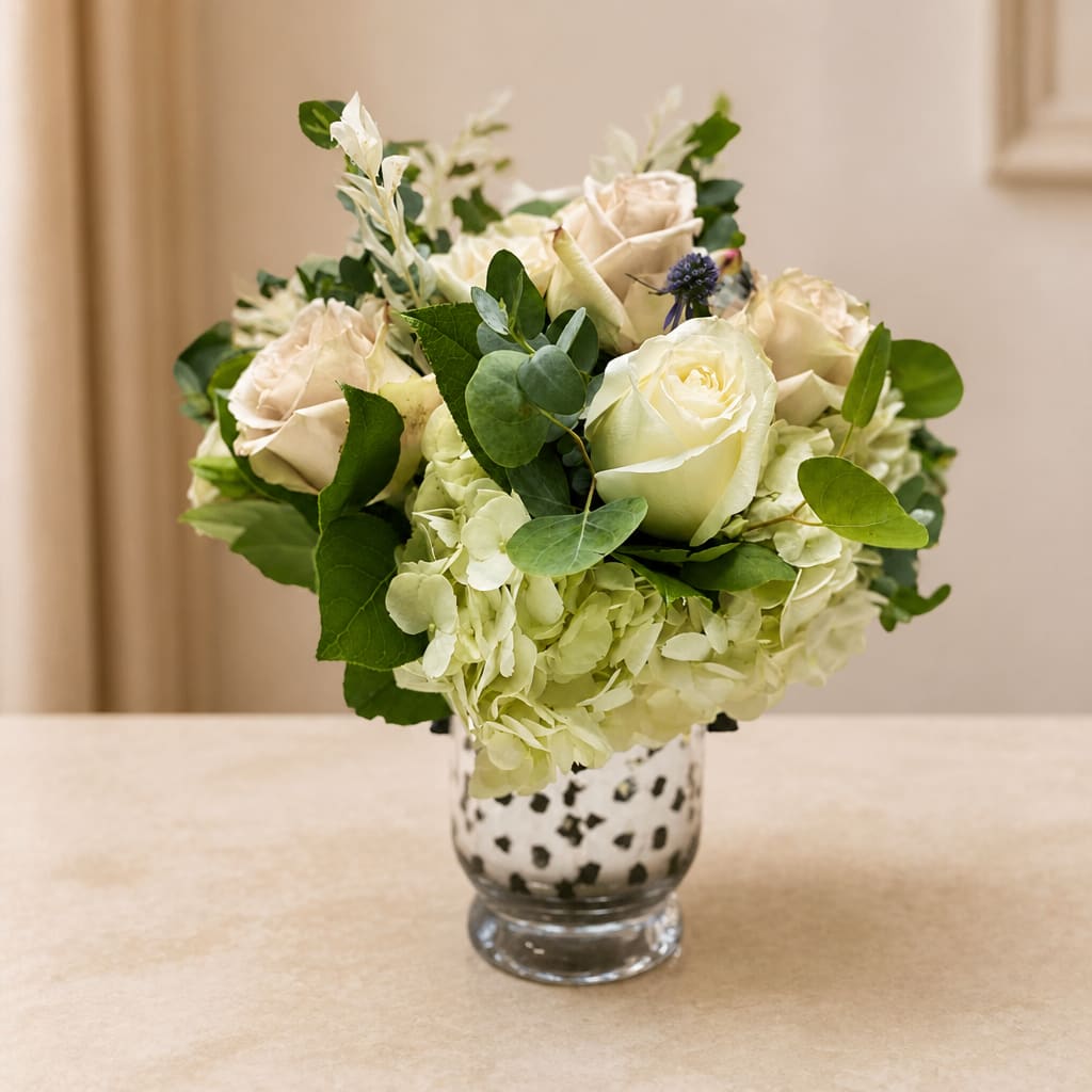 White roses and hydrangeas in a spotted glass vase