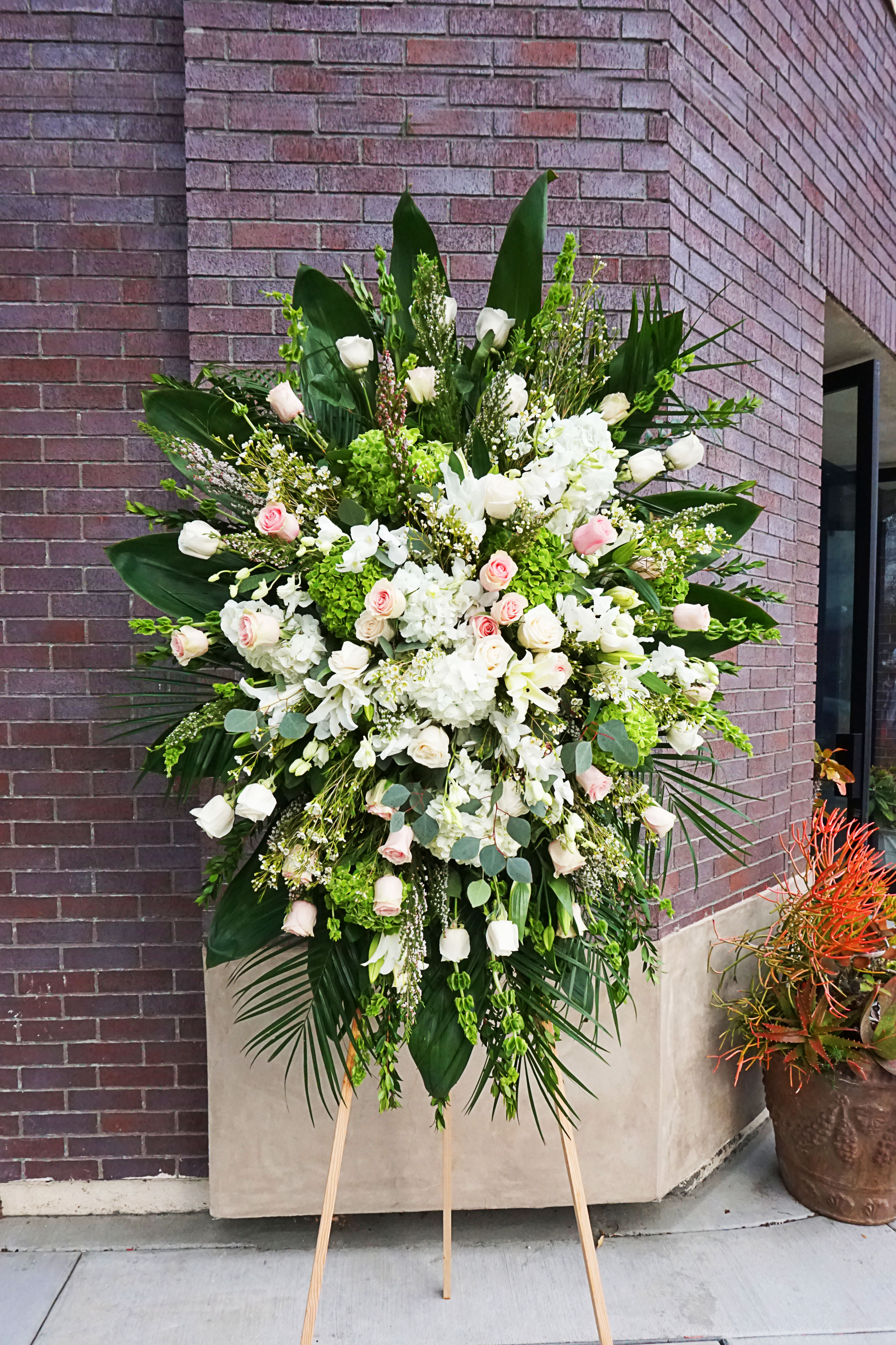Tall standing spray of white hydrangeas and pale pink and white roses on a wooden easel