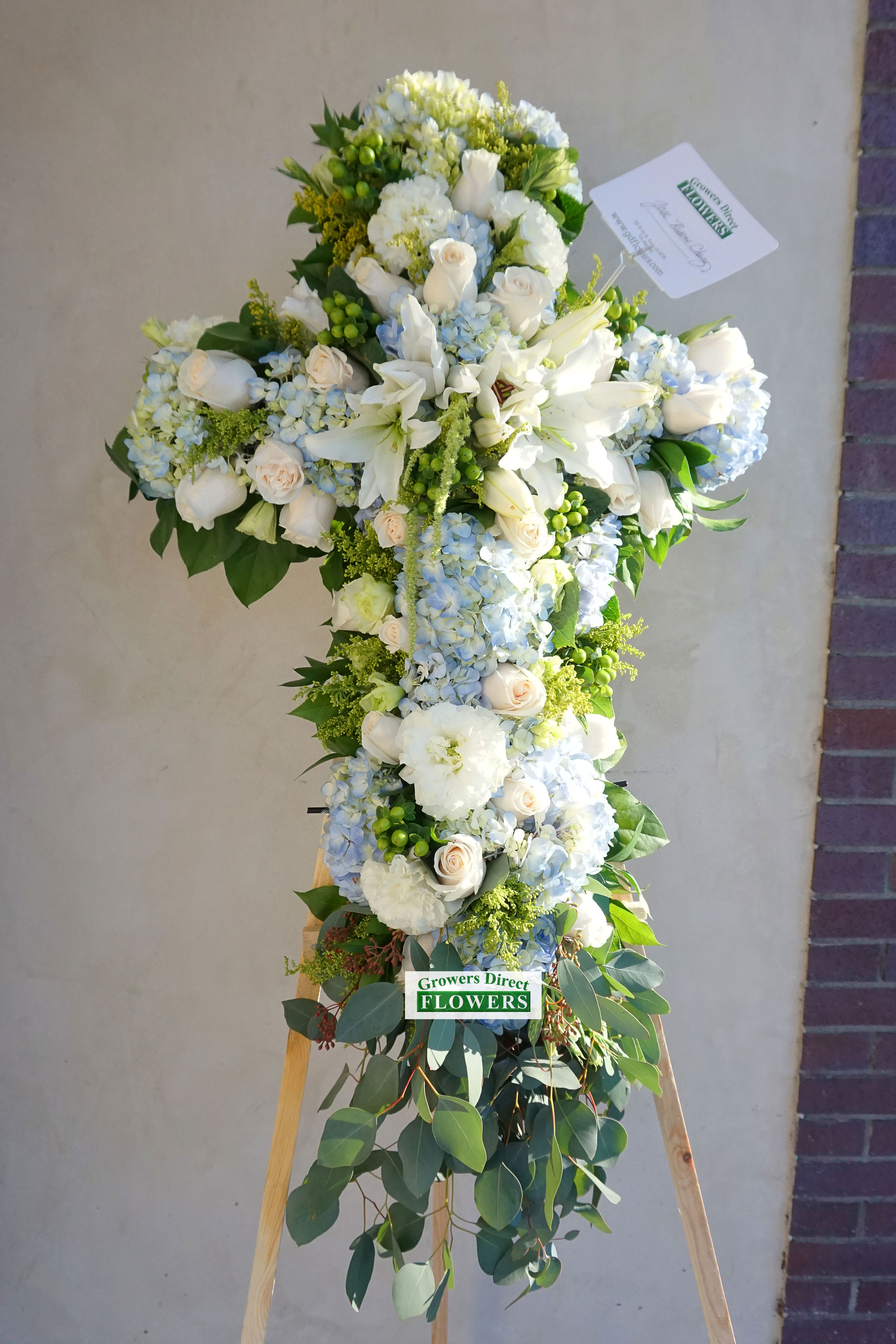 Standing cross-shaped spray of white and pale blue flowers on an easel