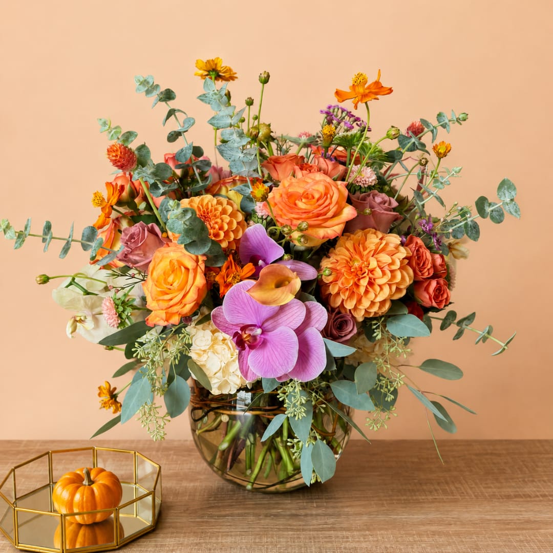 Mixed orange and purple flower arrangement in a glass vase with eucalyptus