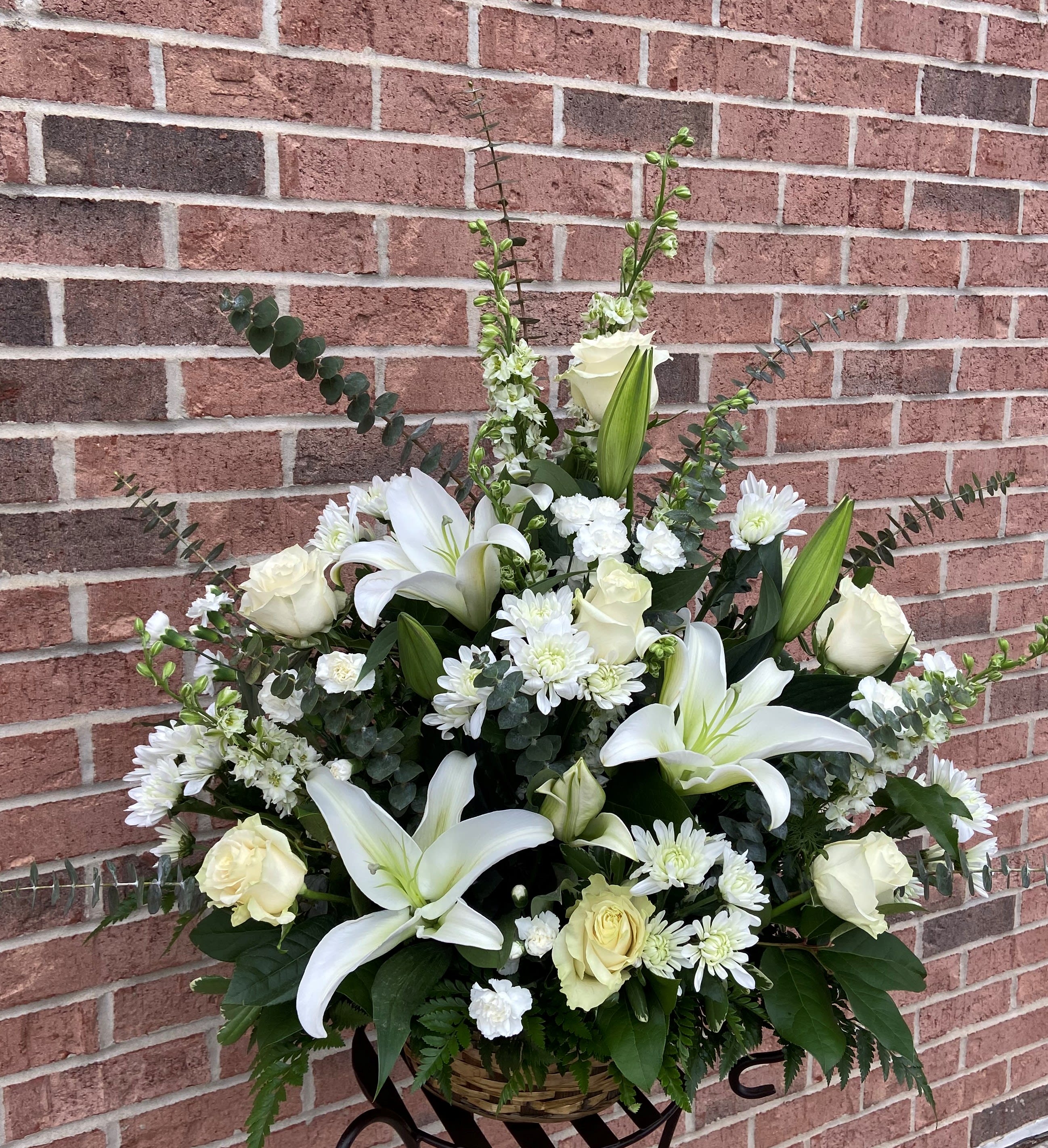 White lilies and roses in a basket arrangement with white daisies