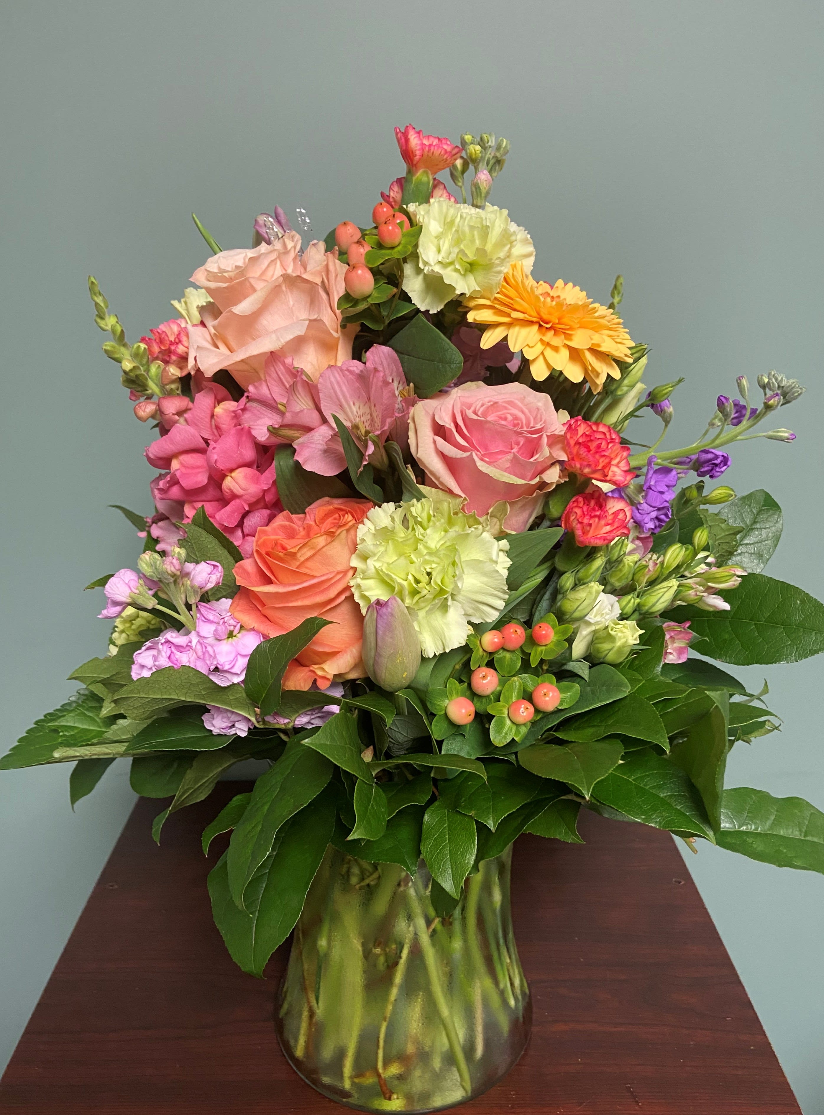 Mixed bouquet of pink, peach, yellow, and purple flowers in a glass vase