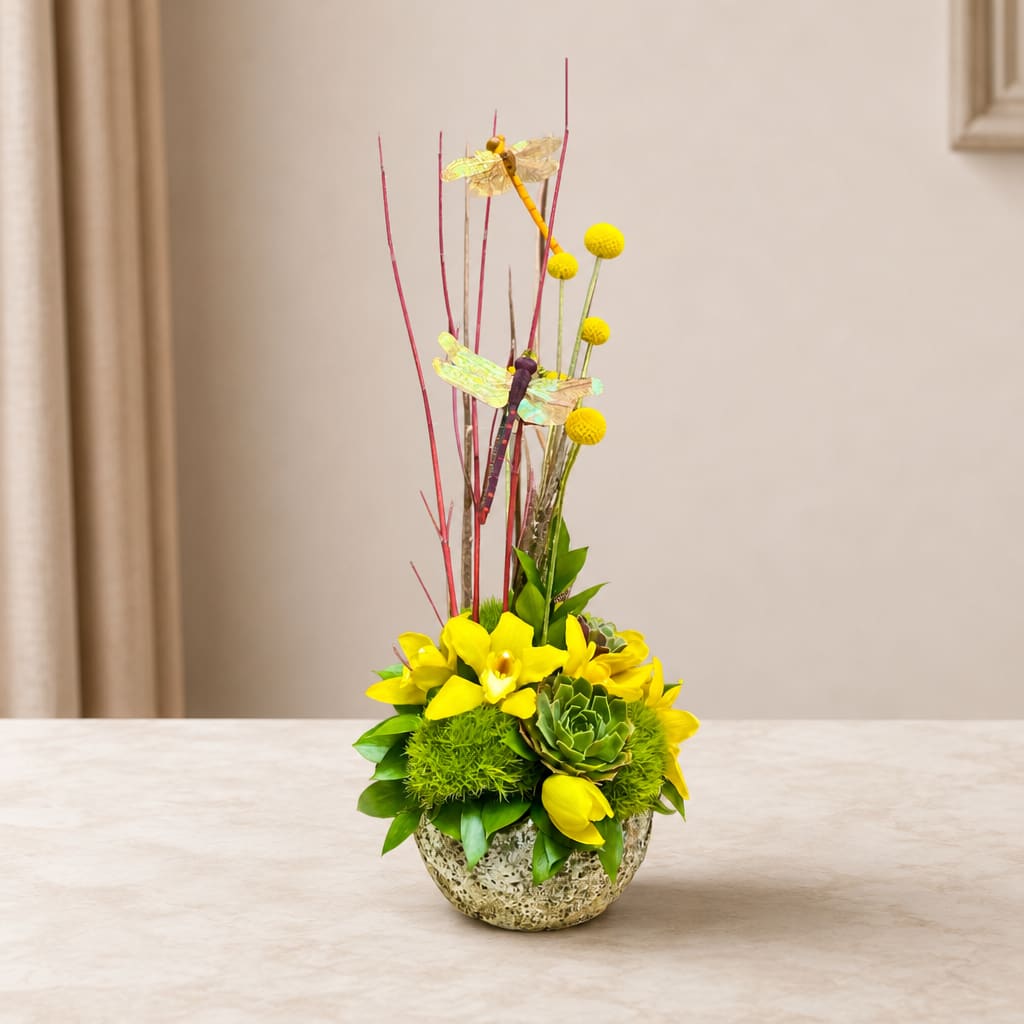Yellow floral arrangement with tall dragonfly picks in a textured bowl