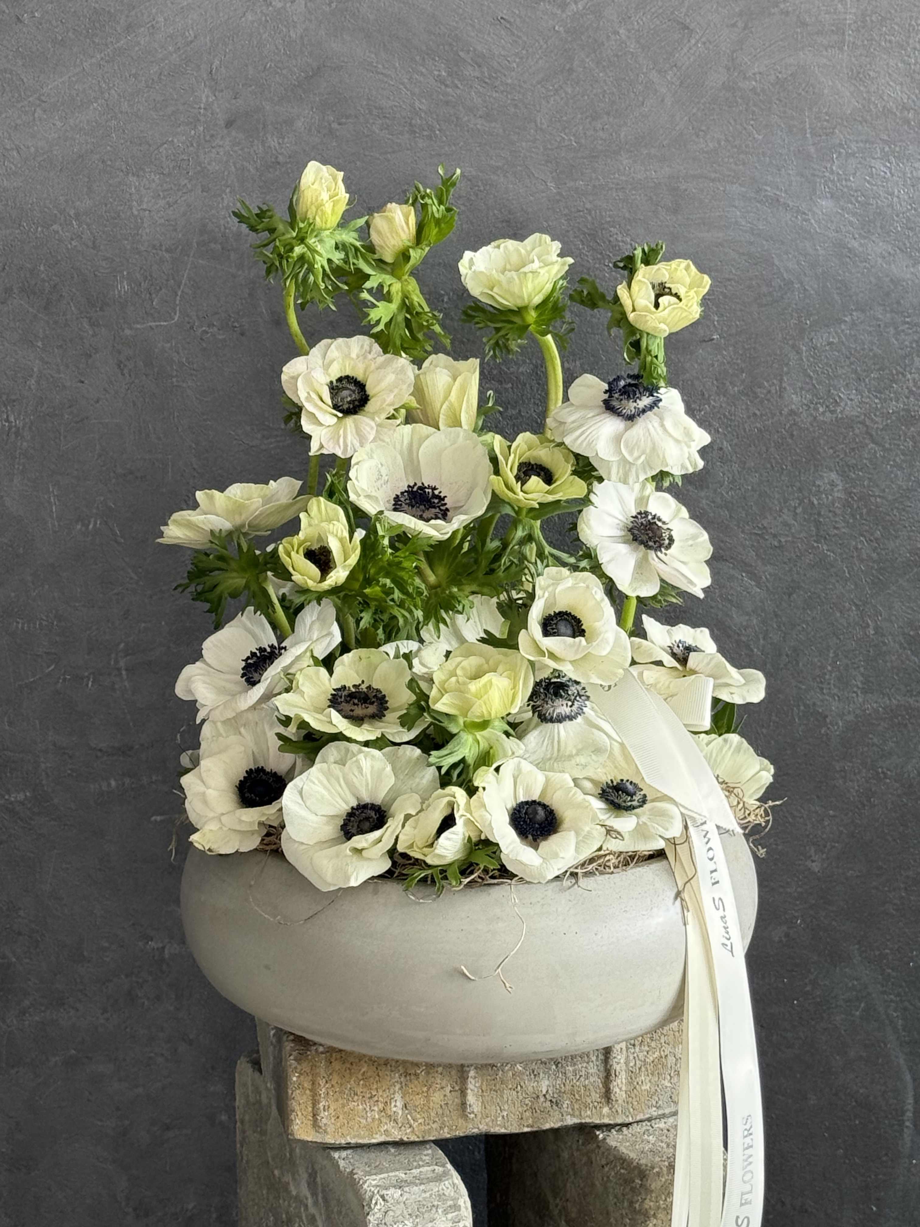 White anemone arrangement in a round gray container with a ribbon