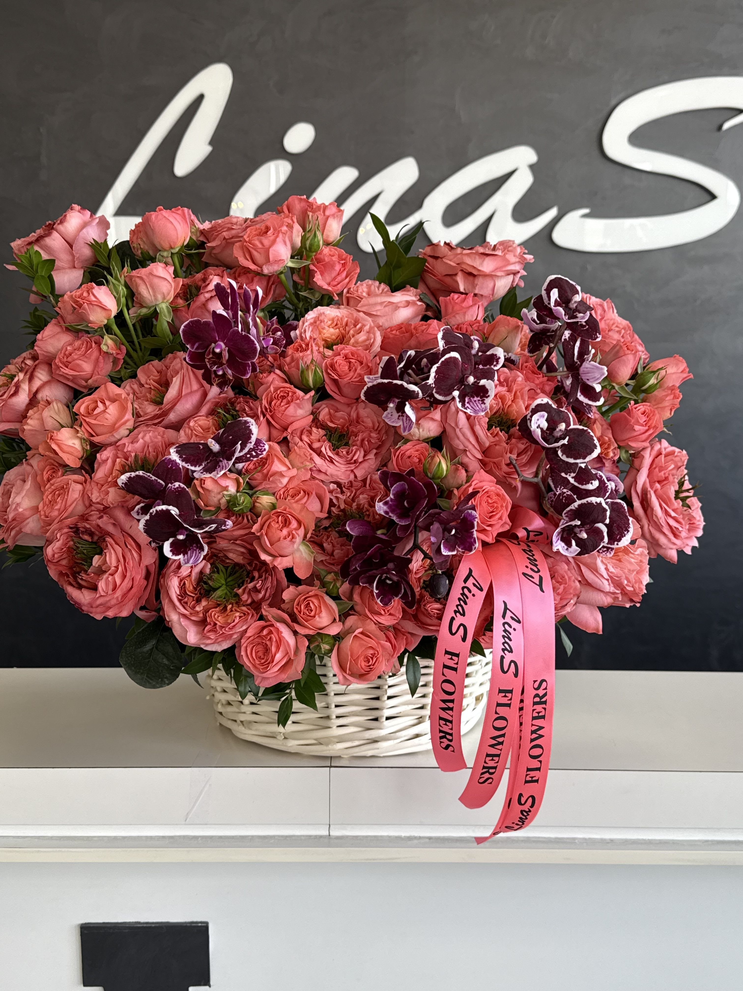 Pink rose bouquet with dark purple orchids in a white basket