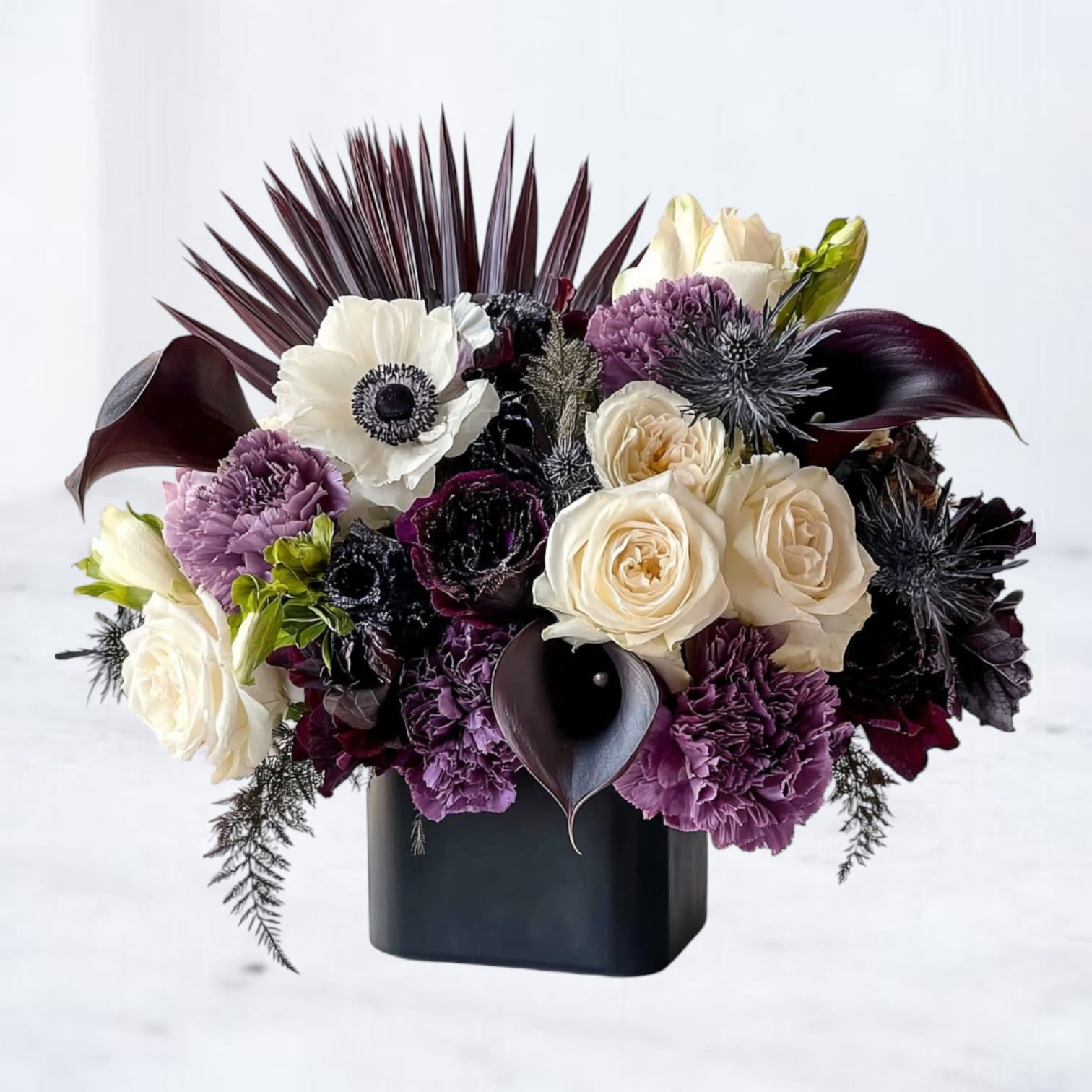 Cream and purple flowers arranged in a black vase with dark foliage