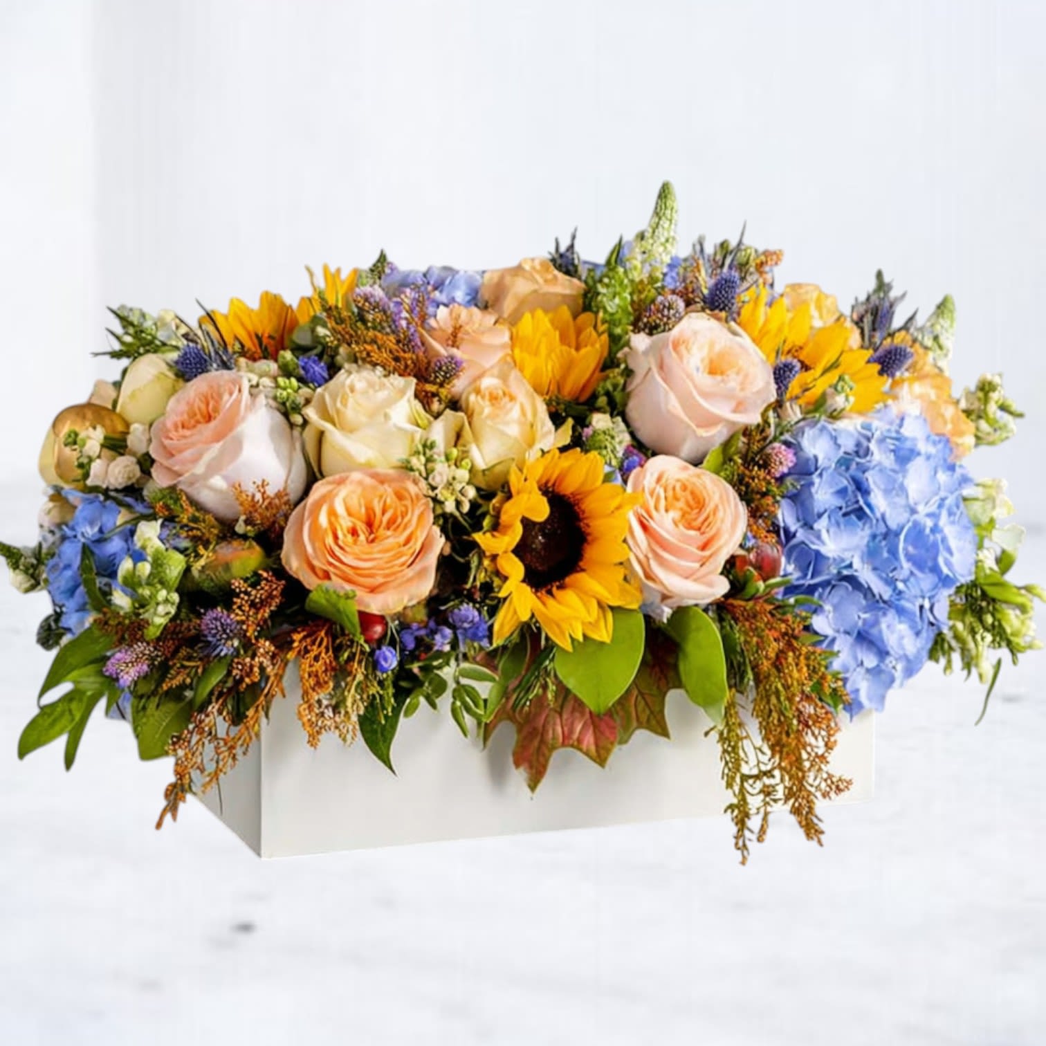 Mixed bouquet with roses, sunflowers, and blue hydrangeas in a white box