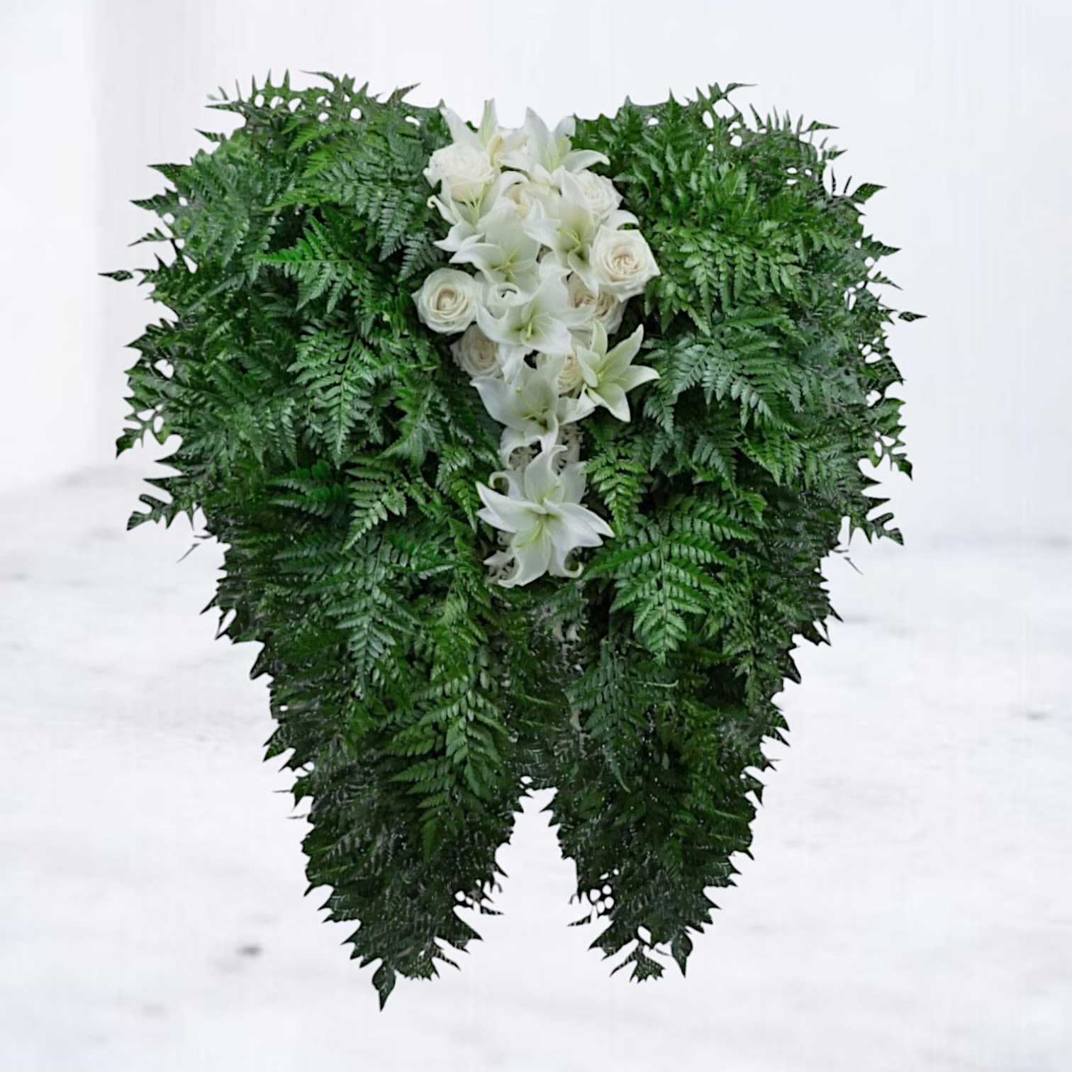 White lilies and roses arranged in a dense green standing spray