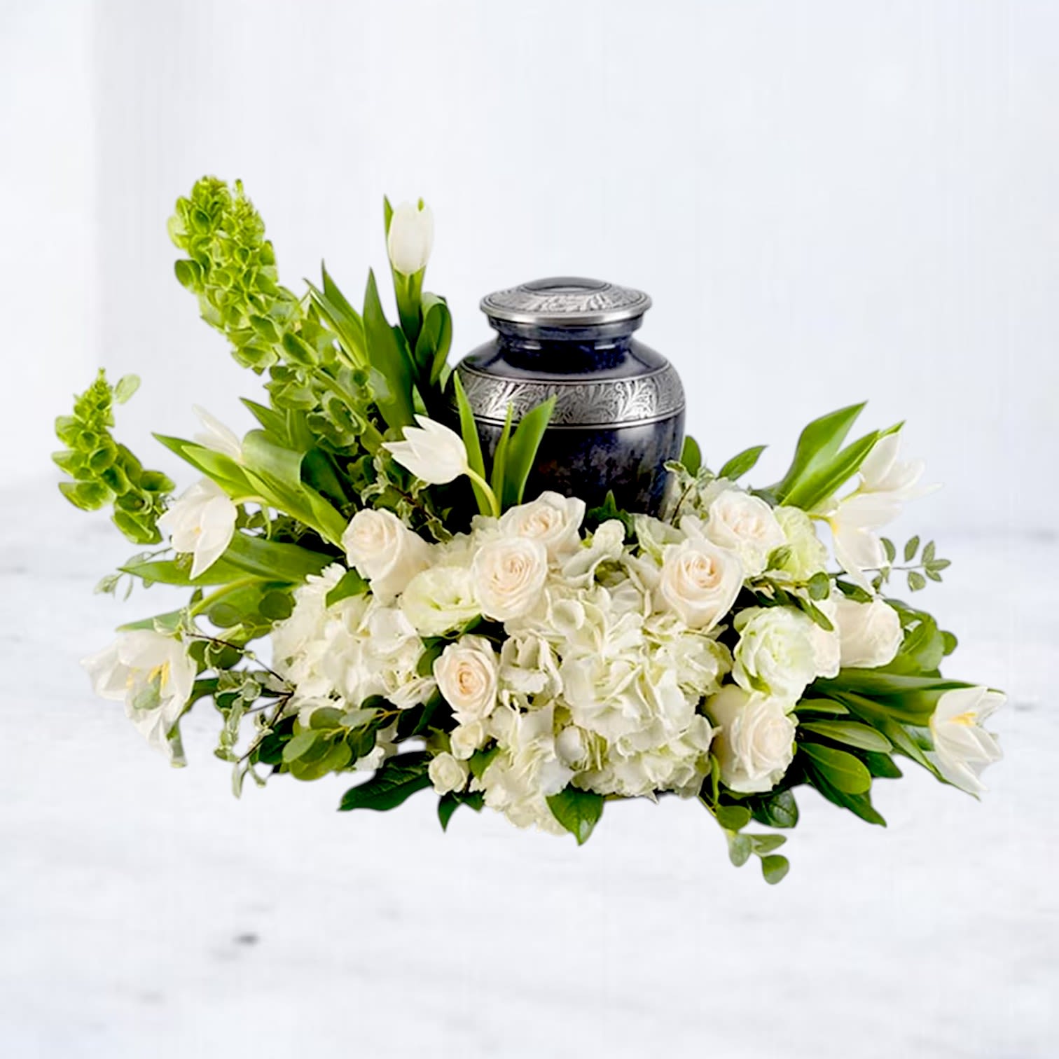 Afterlight - Afterlight is a modern urn surround designed with white hydrangea, premium white roses, tulips, lisianthus, and fresh seasonal greenery in a soft asymmetrical composition surrounding a cremation urn. Designed with movement, texture, and a peaceful neutral palette, this arrangement creates a clean and contemporary tribute while honoring a loved one with elegance and care.  Its airy white florals and fresh green accents offer a serene, garden-inspired aesthetic suited for memorial services, celebration of life ceremonies, funeral displays, or private home remembrance. Designed to complement a variety of urn styles, Afterlight brings softness, warmth, and natural beauty to meaningful spaces.  Available for same-day sympathy flower delivery in Magnolia, TX and surrounding areas including The Woodlands, Montgomery, Conroe, Spring, Tomball, and nearby Lake Conroe communities.
