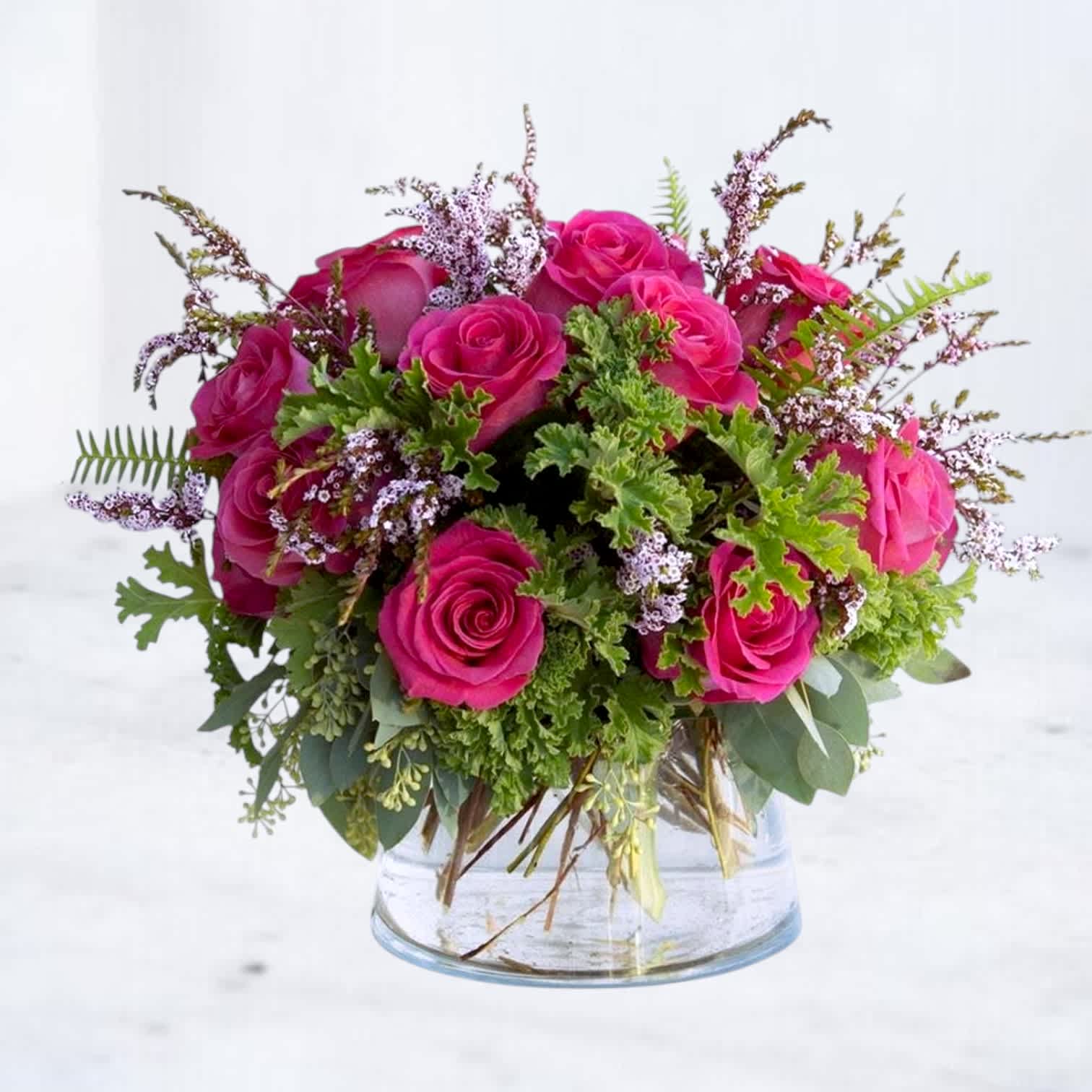 Pink roses arranged in a clear glass vase with greenery and small filler flowers