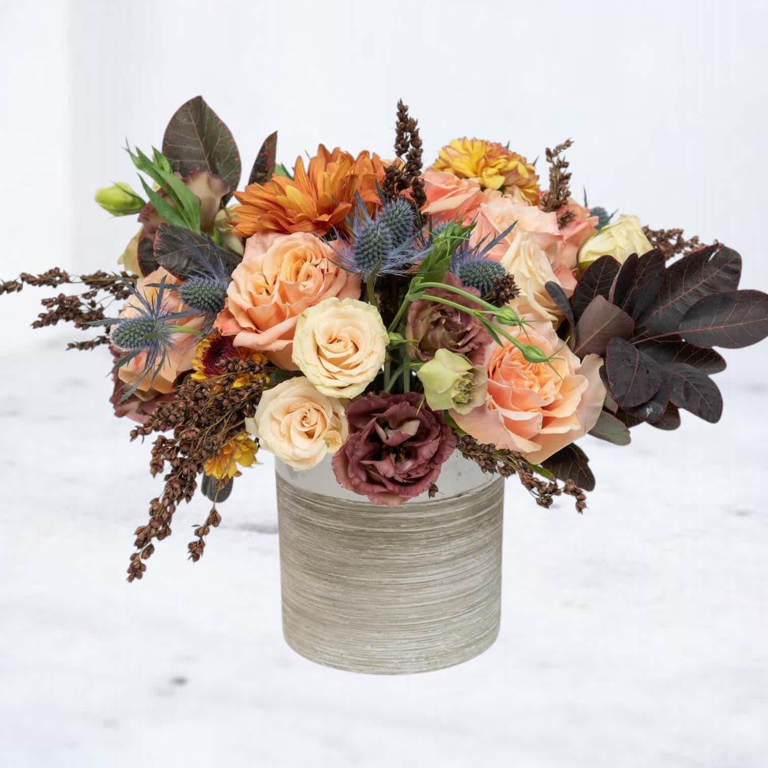 Peach and orange roses with mixed blooms in a cylindrical vase