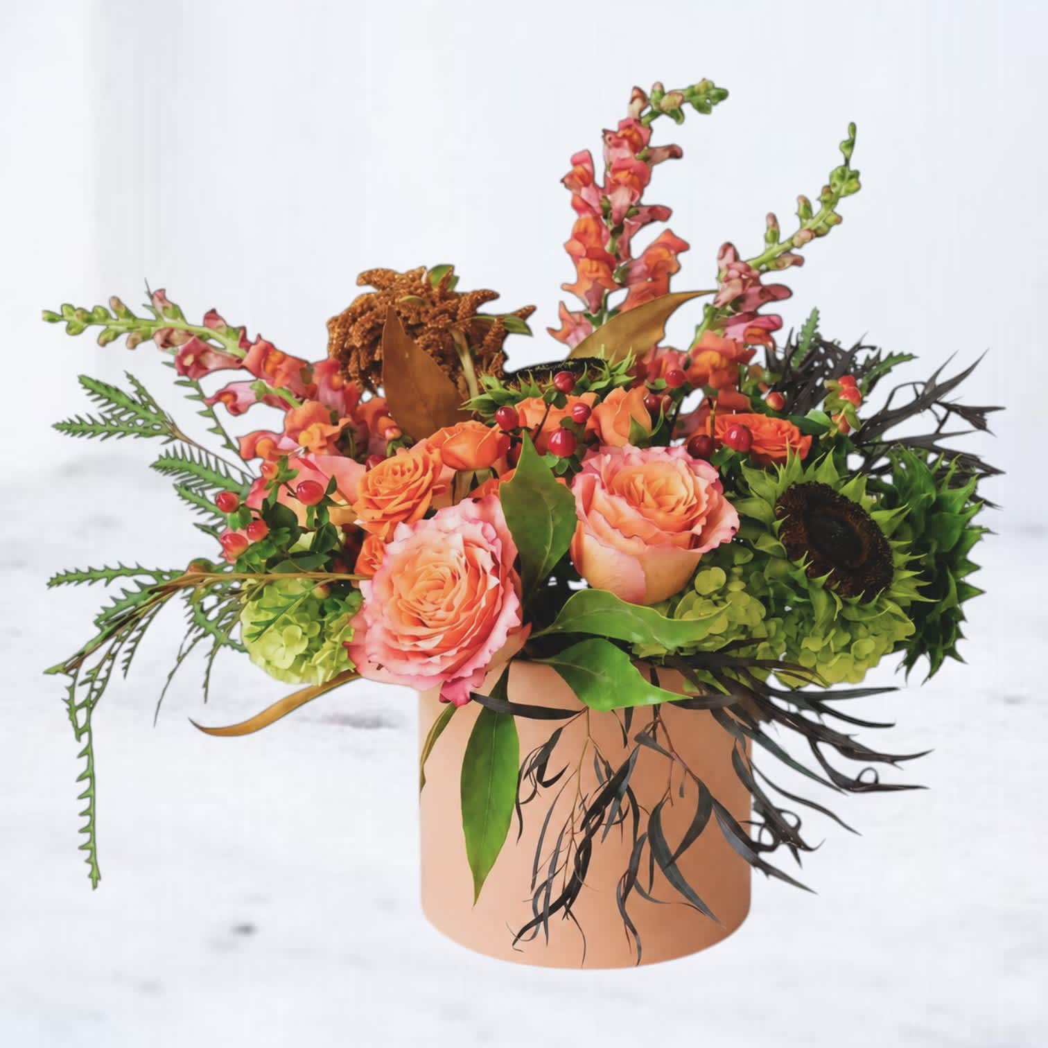 Peach roses and orange snapdragons in a round vase with mixed foliage