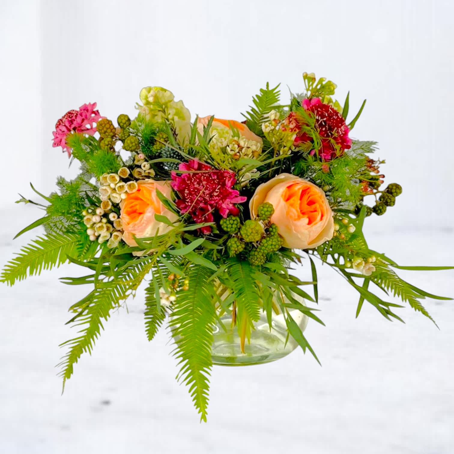 Mixed bouquet of peach roses and pink flowers in a glass vase