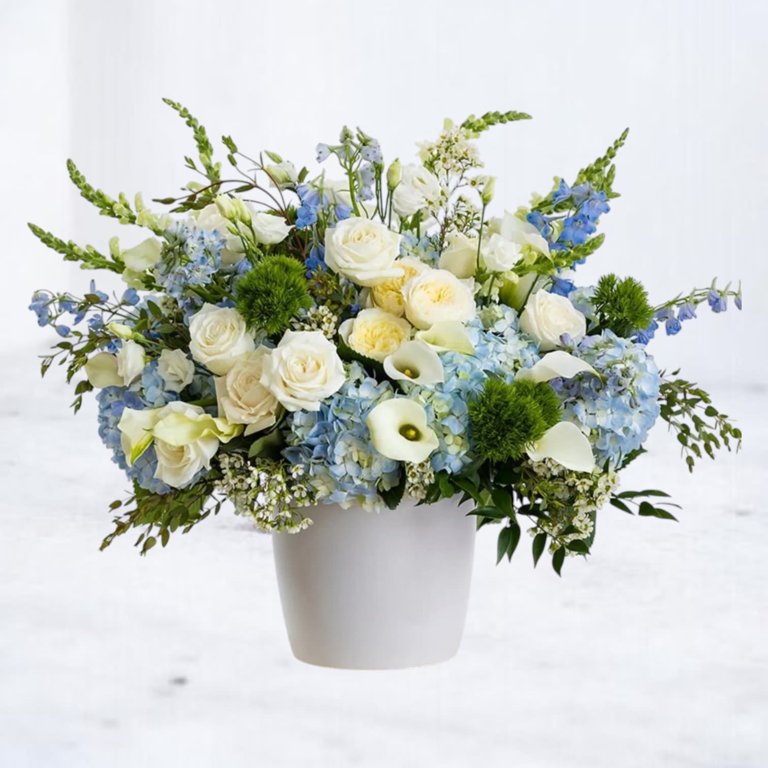Skies &amp; Sunshine - Skies &amp; Sunshine is a fresh, uplifting floral arrangement designed with soft texture, airy movement, and a calming yet radiant color palette. Featuring premium blue hydrangea, creamy white roses, delicate white calla lilies, and soft seasonal blooms, this arrangement is layered with fresh greenery to create a full, garden-inspired composition.  Designed in a modern white vessel, Skies &amp; Sunshine blends cool sky blues with warm creamy whites and soft greens for a look that feels peaceful, refreshing, and naturally elegant. The balance of hydrangea, roses, and airy accent flowers gives this design a light, open feel while maintaining a lush, premium presence.  Perfect for sympathy flowers, get well wishes, birthdays, or sending a thoughtful “thinking of you,” this blue and white flower arrangement offers a serene, uplifting style for any occasion.  Same-day flower delivery is available in Magnolia, TX, The Woodlands, Montgomery, Conroe, Spring, Tomball, and surrounding North Houston areas.  Due to seasonal availability, some blooms may be replaced with similar varieties of equal or greater value to maintain the design’s look and integrity. Your arrangement will always reflect the same color palette, style, and premium quality.