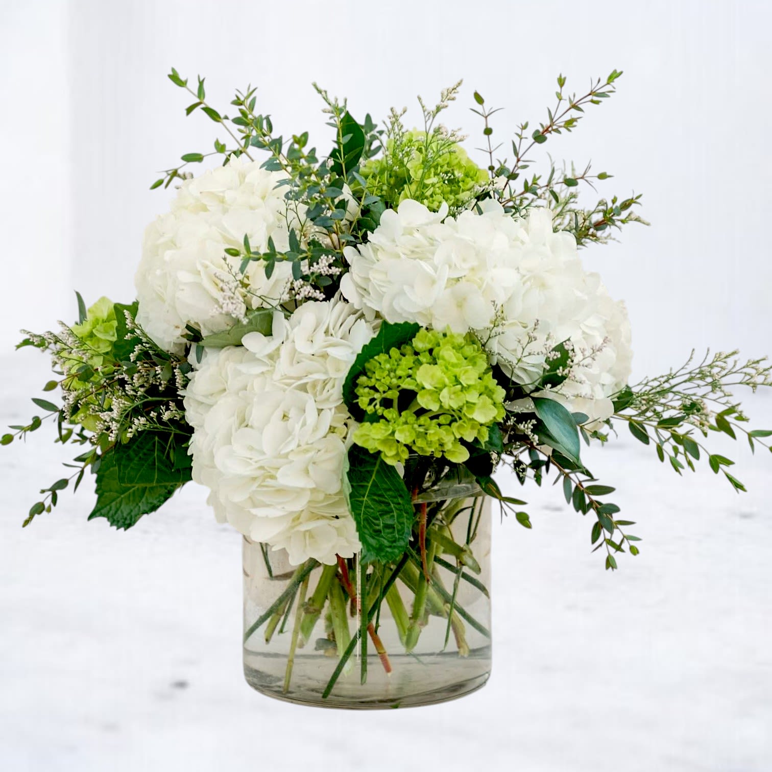 Northwind - Fresh, airy, and effortlessly elegant, Northwind brings together lush white hydrangea, vibrant green viburnum, and delicate seasonal greenery in a design inspired by nature's quiet beauty.  Designed with layers of texture and movement, this arrangement features cloud-like blooms accented by fresh green tones and graceful botanical elements. The result is a clean, sophisticated composition that feels both timeless and modern.  Arranged in a clear glass vase, Northwind offers a versatile style that complements any space, making it an ideal gift for birthdays, sympathy occasions, housewarmings, thank-you gifts, celebrations, or simply brightening someone's day.  Each arrangement is handcrafted by the designers at Whiskey Wallflower using the freshest flowers available. While flower varieties may vary based on seasonal availability, the overall style, color palette, and value will remain true to the design shown.  With its fresh palette and natural elegance, Northwind delivers beauty that feels effortless, refined, and welcoming.