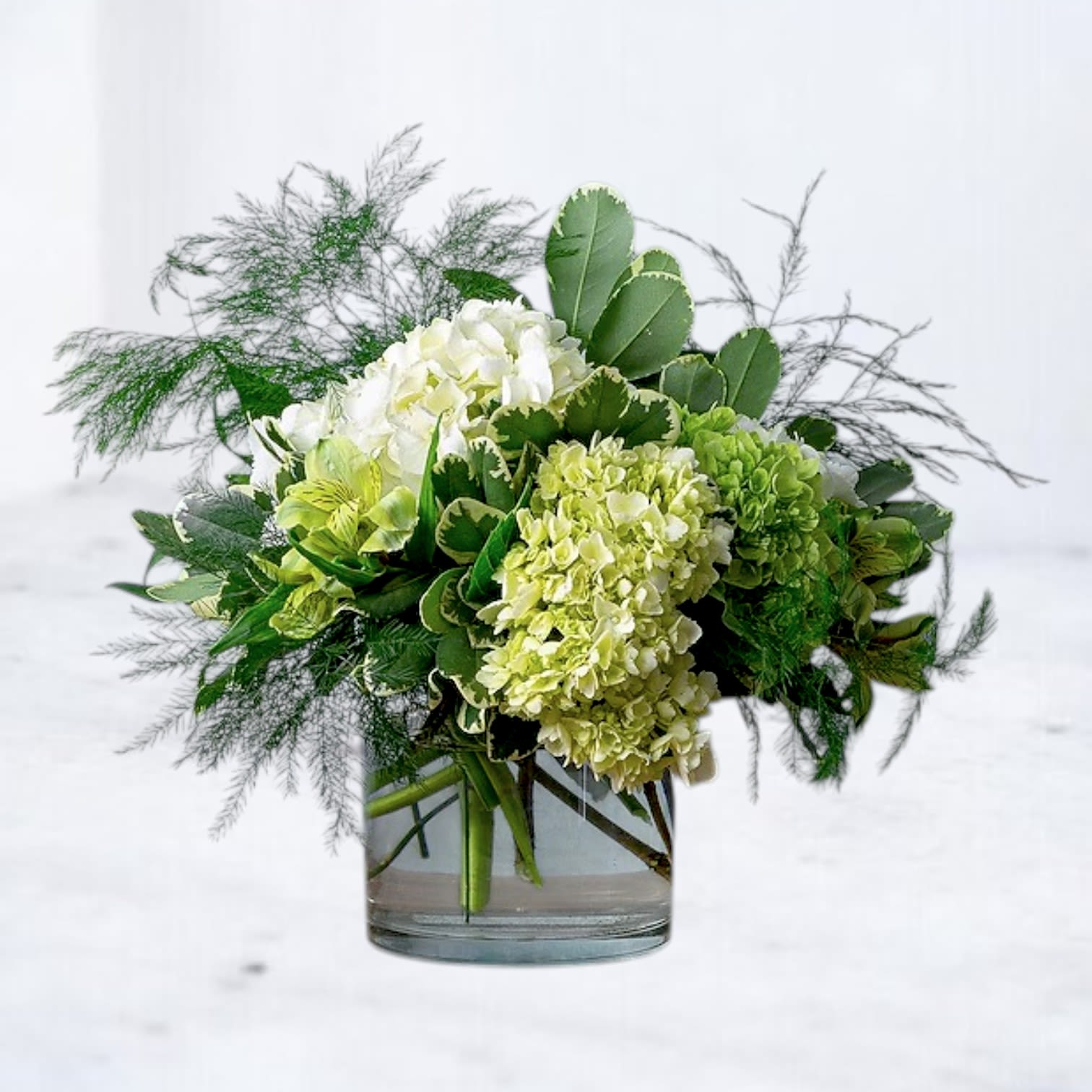 Open Still - Open Still is a softly composed arrangement designed to feel calm, natural, and thoughtfully balanced. Featuring a refined mix of seasonal white blooms, fresh green accents, and airy textural elements, this design has an effortless presence that suits a wide range of moments.  Equally appropriate for sympathy, birthdays, thank-you gestures, or just because, Open Still offers a sense of ease and quiet beauty without feeling formal or heavy. Arranged in a clear glass vessel, it brings a light, modern touch to any space.  Designed with seasonal blooms; exact flowers may vary to ensure the freshest selection while preserving the overall look and tone of the arrangement.
