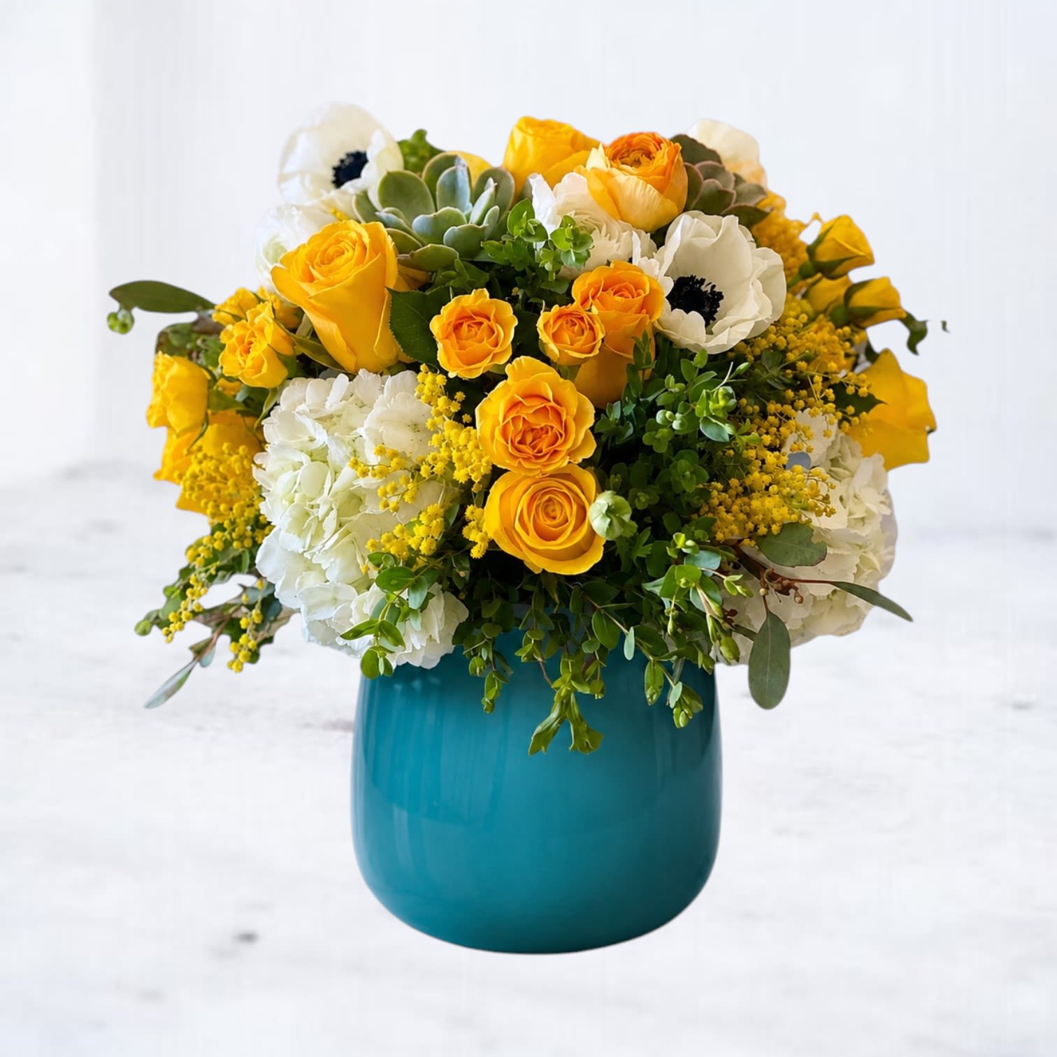 Fulgent Oasis - Radiate warmth and joy with the Fulgent Oasis floral arrangement. This stunning bouquet showcases vibrant yellow roses, cheerful spray roses, elegant ranunculus, and lush hydrangeas, artfully accented with fresh greenery and soft blooms. Nestled in a striking teal vase, this arrangement exudes modern elegance and charm, perfect for brightening any space or celebrating life's special moments. Fulgent Oasis is the ultimate gift to make someone’s day shine. Order now and bring the beauty of sunshine into your home or theirs!