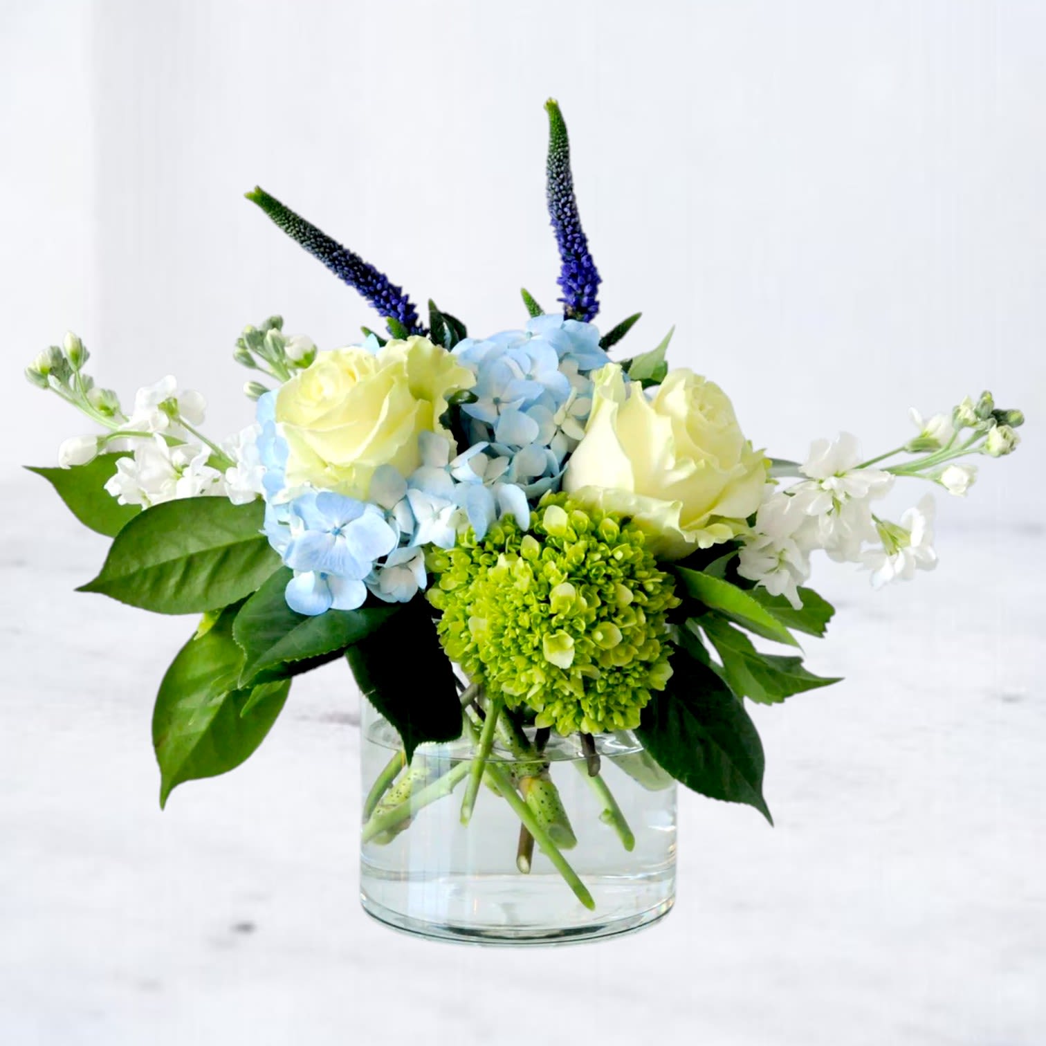 Quiet Current - Send a thoughtful expression with Quiet Current, a soft and calming flower arrangement designed in shades of blue, white, and fresh green. Featuring premium blooms like hydrangea, roses, lisianthus, and seasonal florals, this garden-inspired design offers a peaceful and elegant way to send sympathy flowers, condolences, or thoughtful support.  Handcrafted by a local florist and available for same-day flower delivery in Magnolia, TX and surrounding areas including The Woodlands, Montgomery, Conroe, Spring, and Tomball, this arrangement is ideal for sympathy deliveries to homes, hospitals, funeral services, or memorial gatherings. Its clean, modern style and soothing color palette create a meaningful gesture that feels refined, comforting, and beautifully understated.  Whether you're sending sympathy flowers, comfort flowers, or a graceful arrangement to brighten someone’s day, Quiet Current is designed with fresh seasonal blooms and an airy, natural style that feels timeless and sincere.