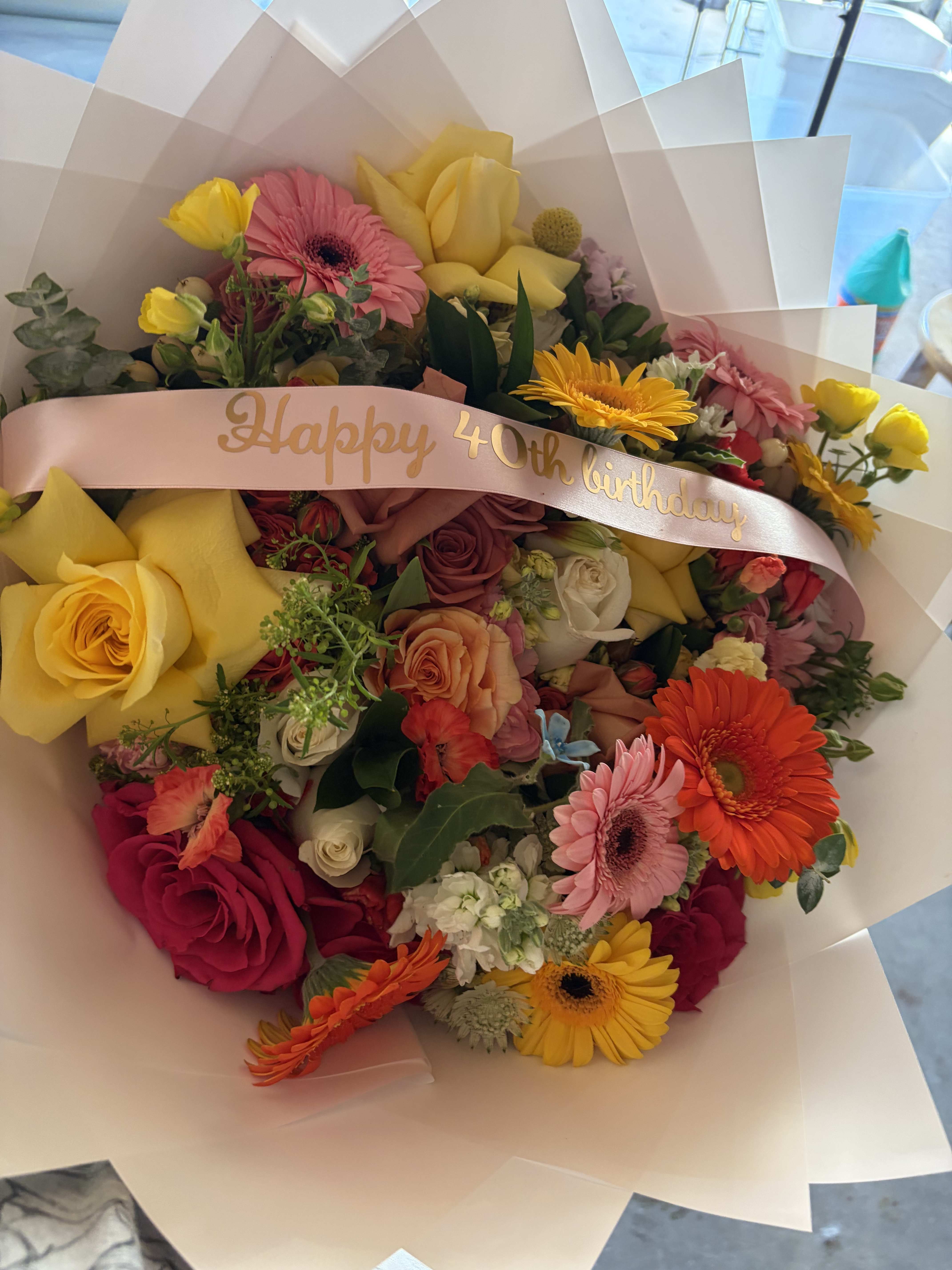 Mixed bouquet with roses, gerbera daisies, and yellow tulips, wrapped with a birthday ribbon