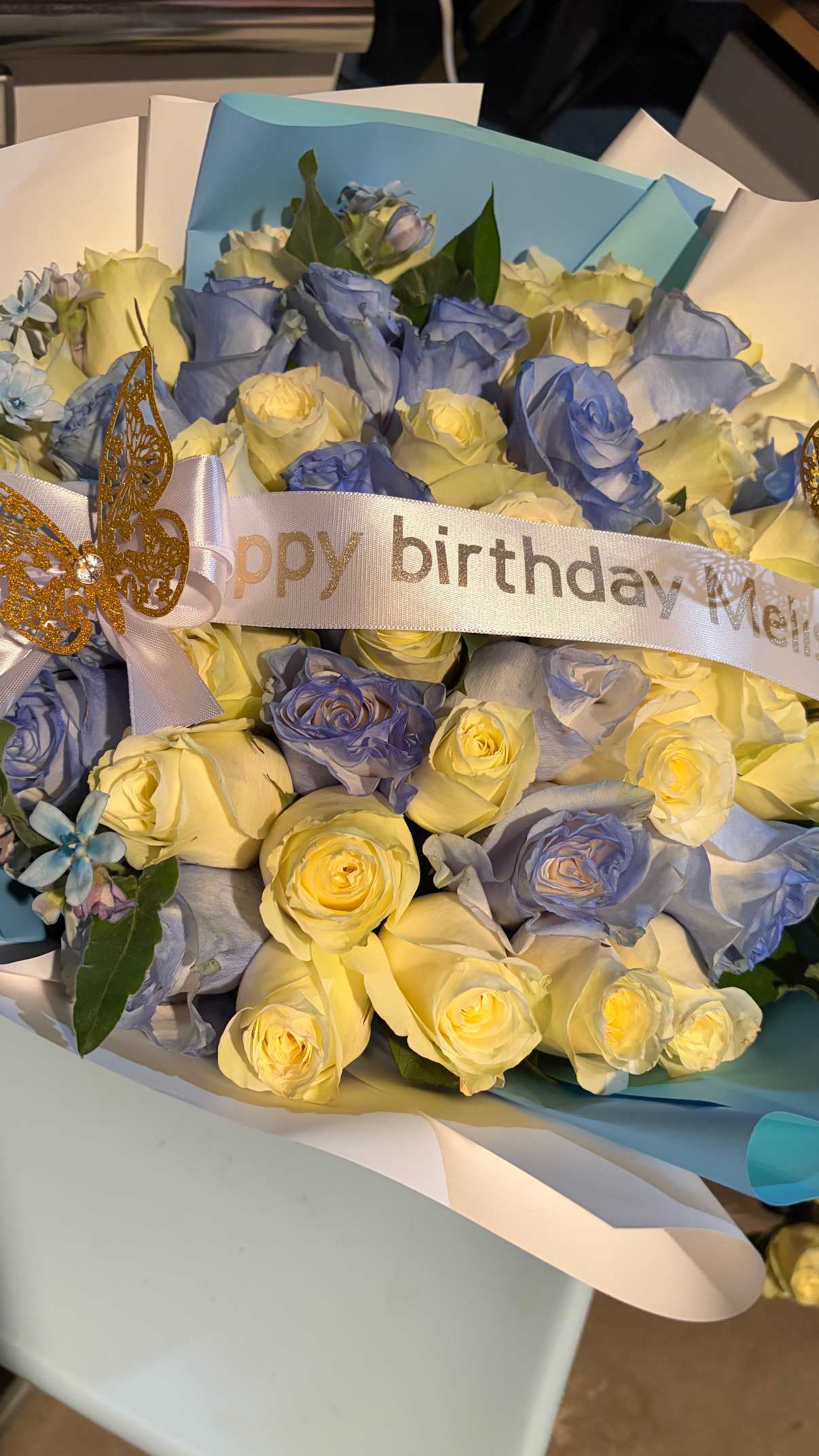 Bouquet of pale yellow and blue roses with a birthday ribbon