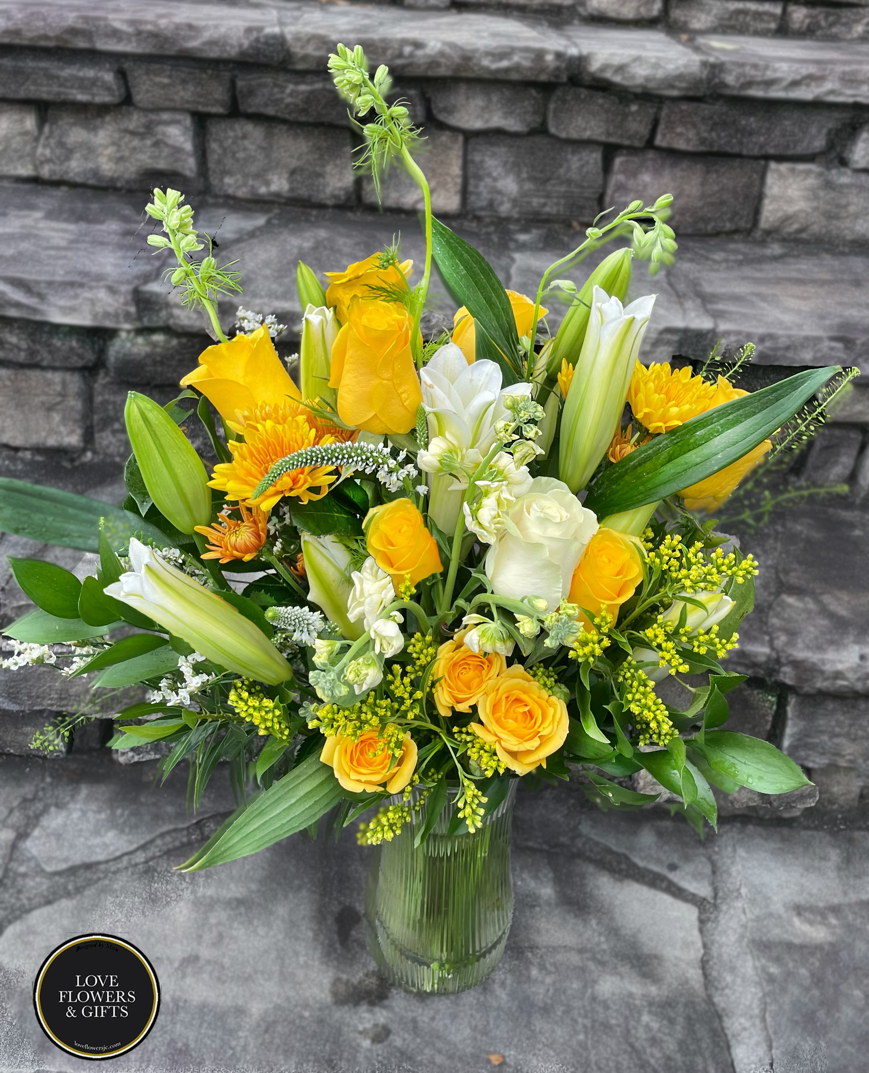 Tall yellow and white arrangement with roses and lilies in a clear glass vase