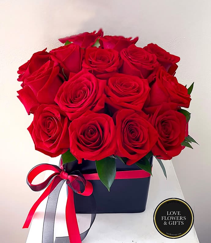 Tight cluster of red roses arranged in a black box with red and black ribbon bow.