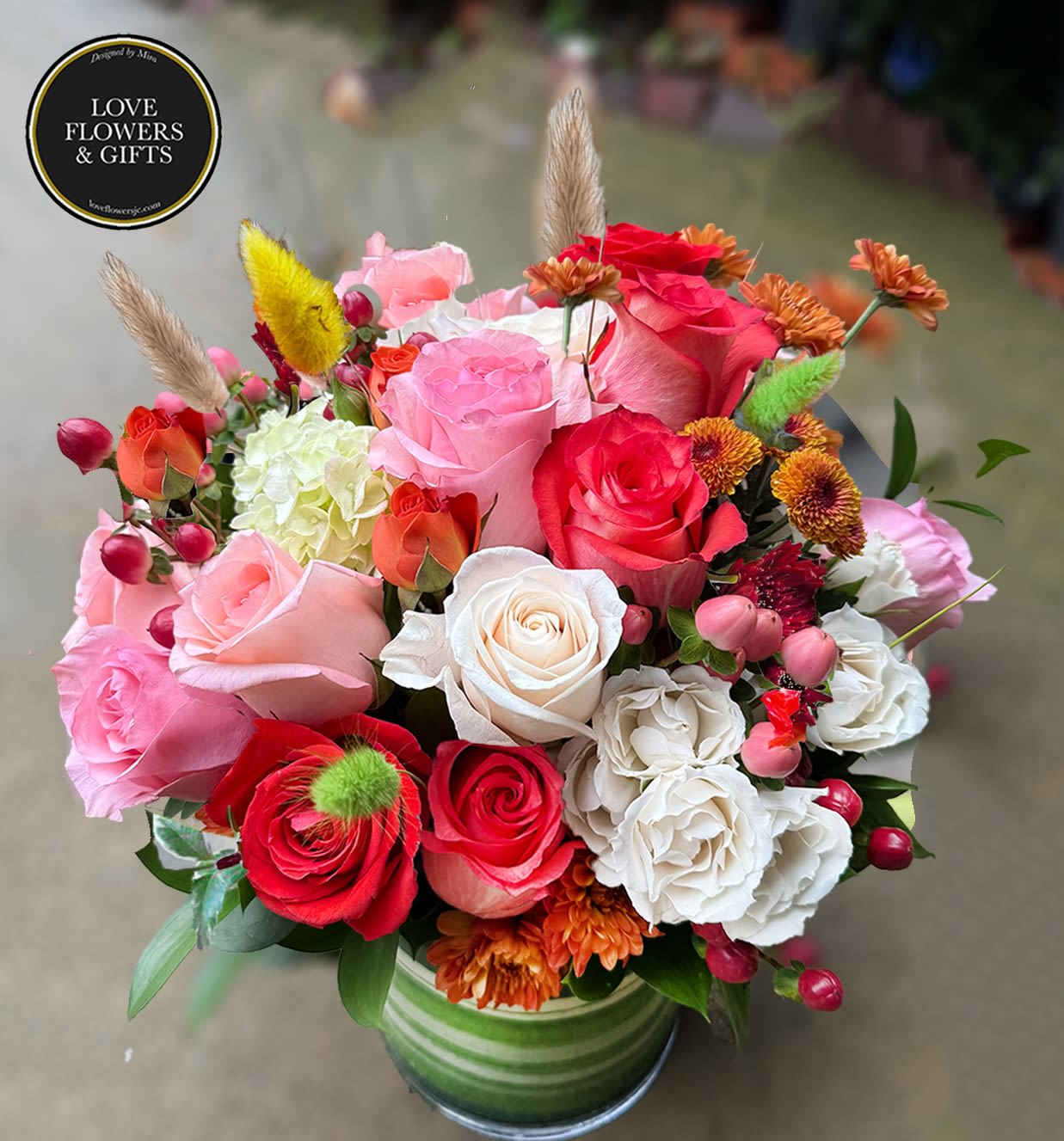Mixed arrangement of pink, red and white roses with accent blooms in a green striped vase