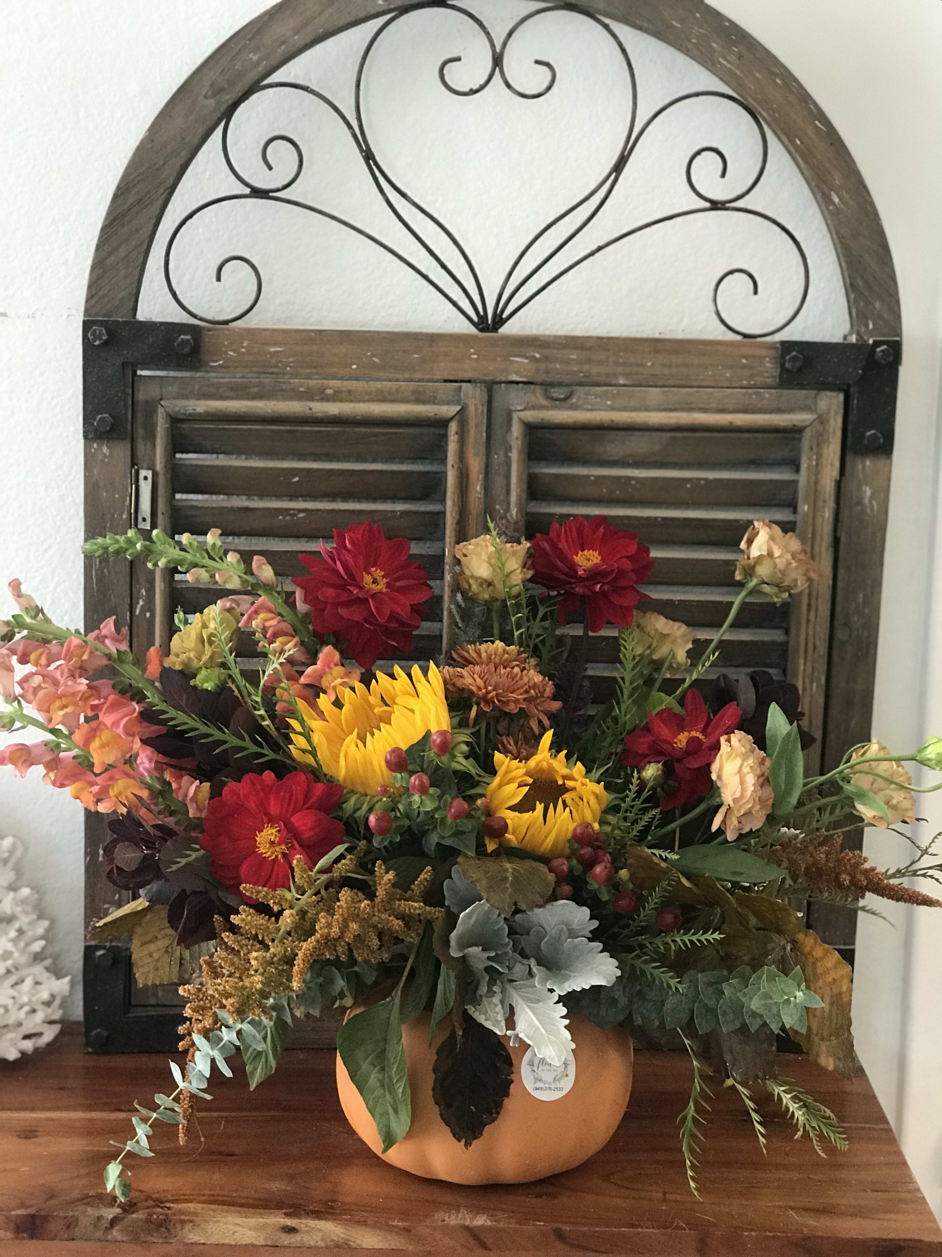 Fall floral arrangement in a pumpkin container with sunflowers and red blooms