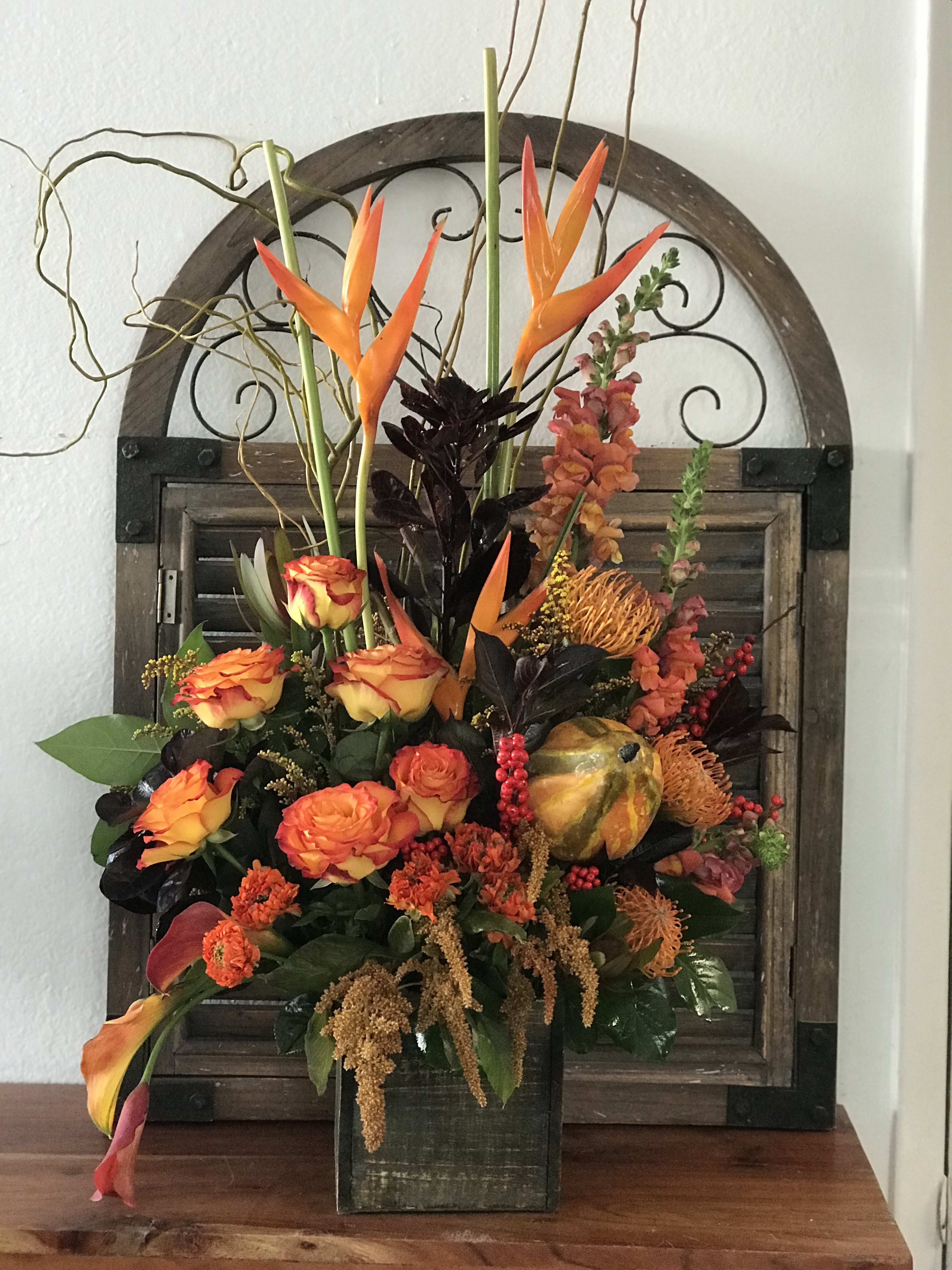 Orange and yellow floral arrangement in a dark vase with tall tropical blooms