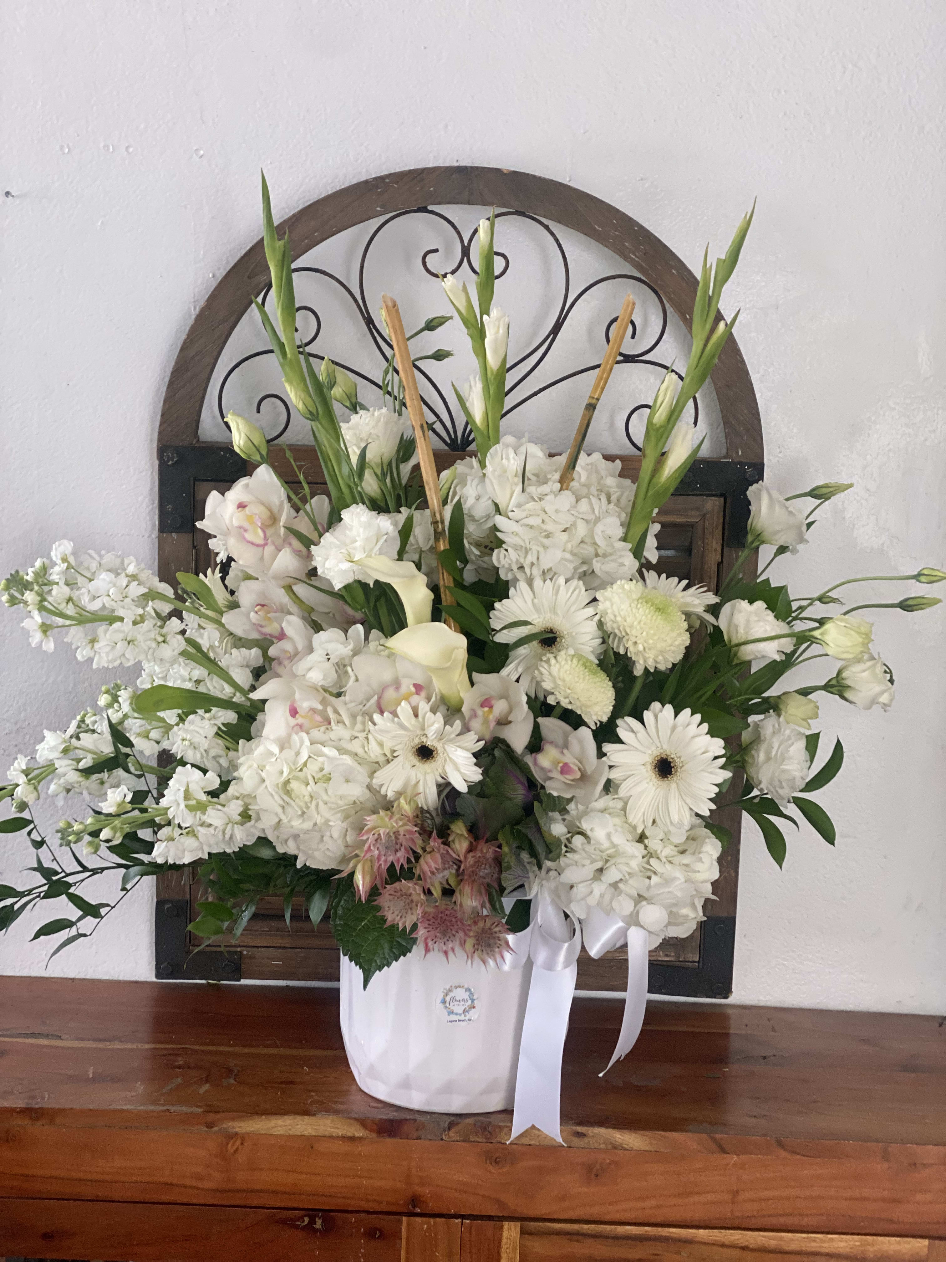 White floral arrangement in a white container with ribbon