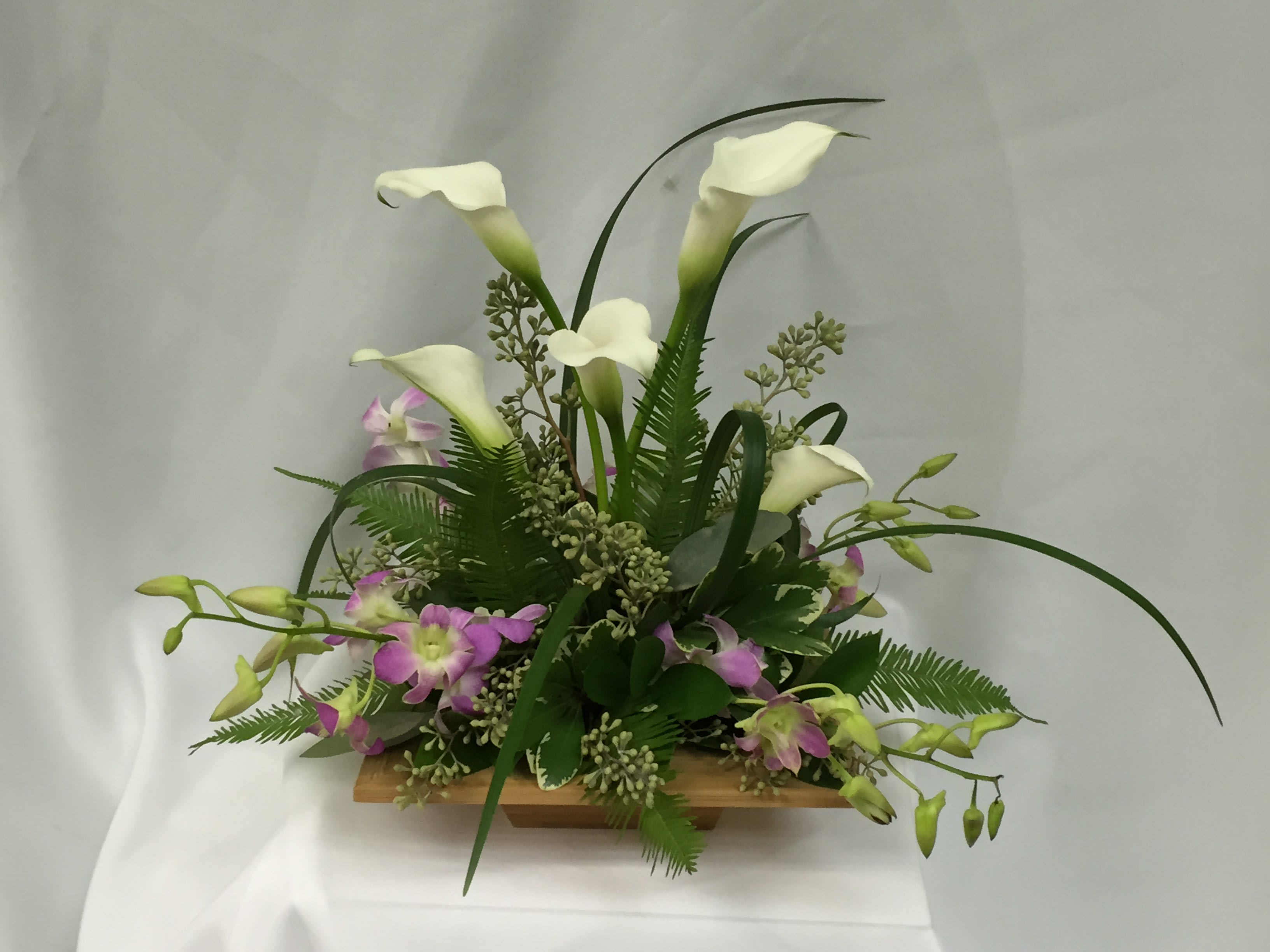 White calla lilies and purple orchids in a low wooden container